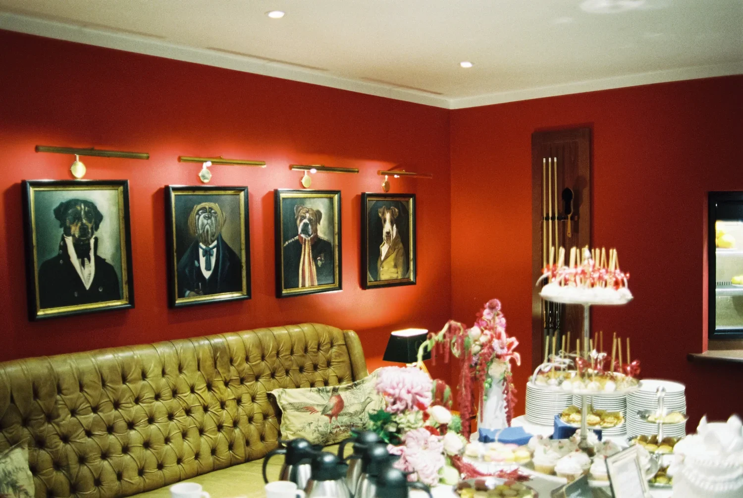 Historical red wall at Schloss Lübbenau with four unique dog portraits in golden frames above a leather sofa.
