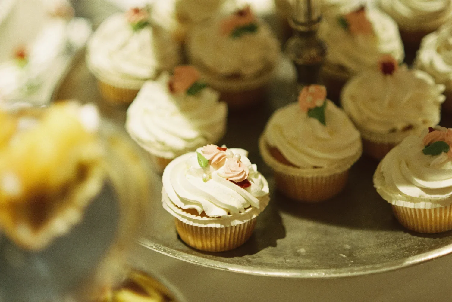 Macro shot of decorated cupcakes on a silver tray, focusing on the texture and analog film grain.