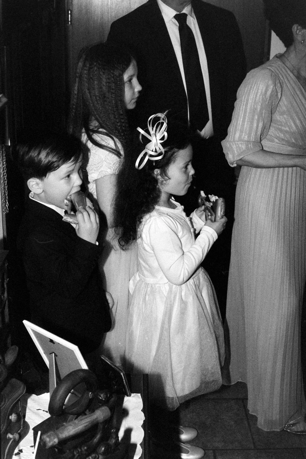 Children in formal outfits enjoy snacks during a wedding, captured with analog documentary photography