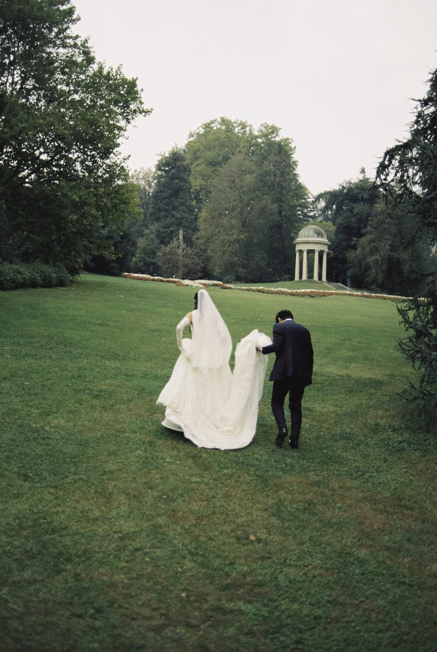 Bride and groom walking through the lush green gardens of Villa Olmo at Lake Como on analog film.