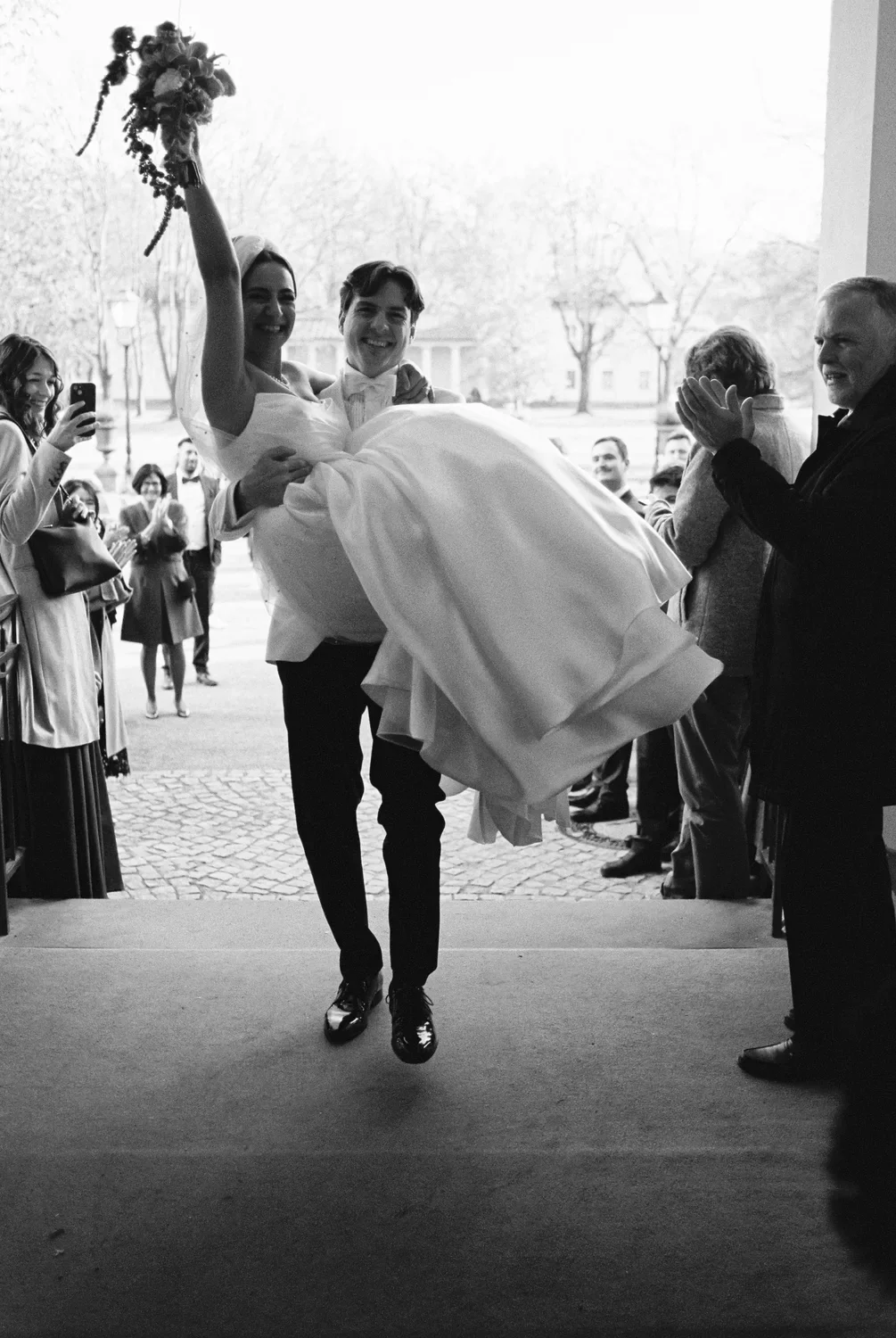 Dynamic black and white 35mm film portrait of a groom carrying his bride, high energy and raw emotion.