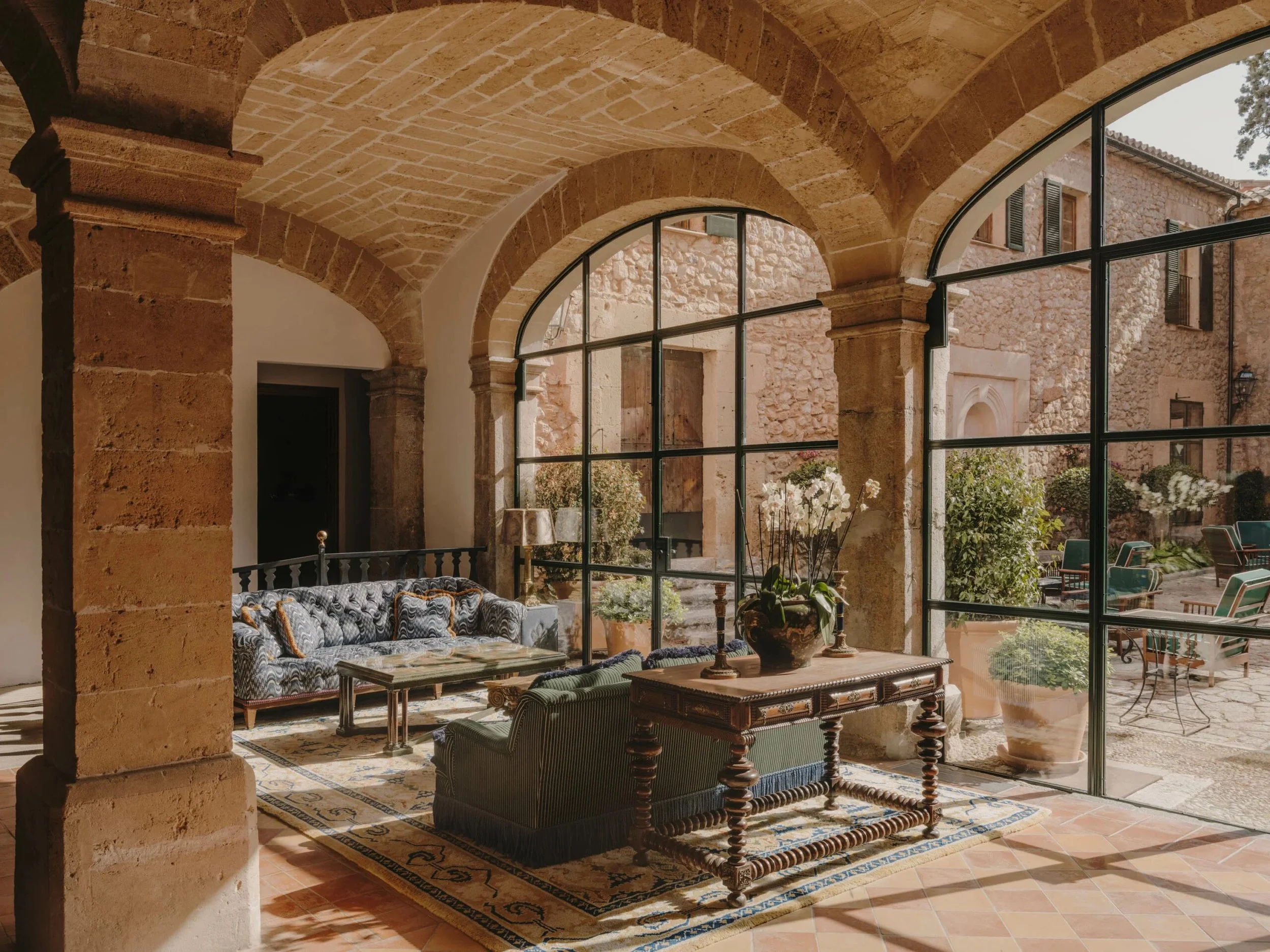 Elegant lounge at Grand Hotel Son Net in Mallorca with stone walls, antique furniture, and large glass windows overlooking the mountains.