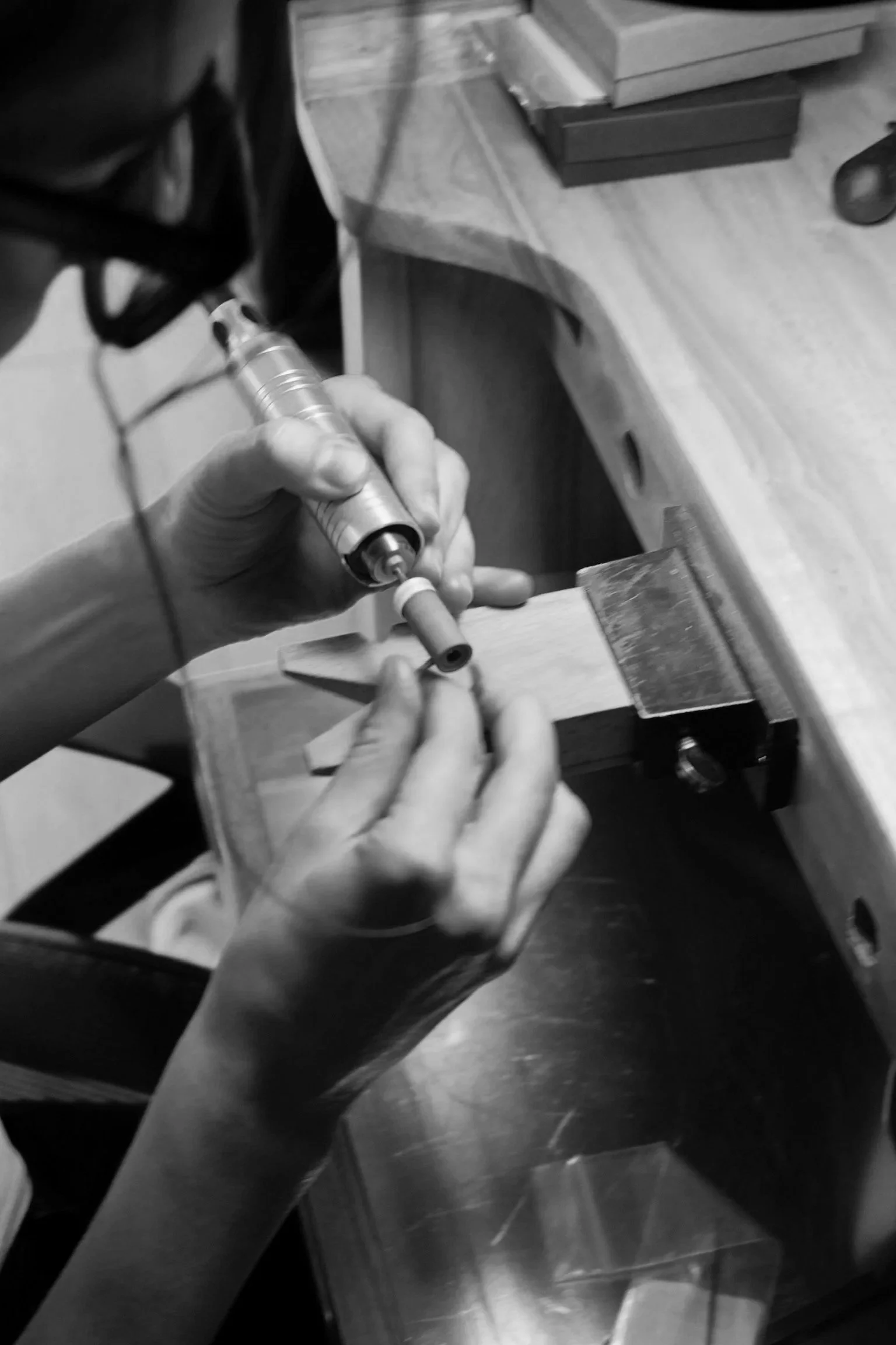 Person holding a rotary tool, engraving or working on a small cylindrical object fixed in a vice on a workbench.