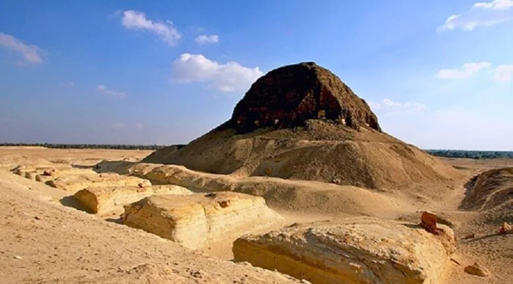 Three women sitting at a table in a restaurant with a rustic wooden ceiling and chandeliers. The woman in the middle and the woman on the right are smiling and looking at each other, while the woman on the left is eating.