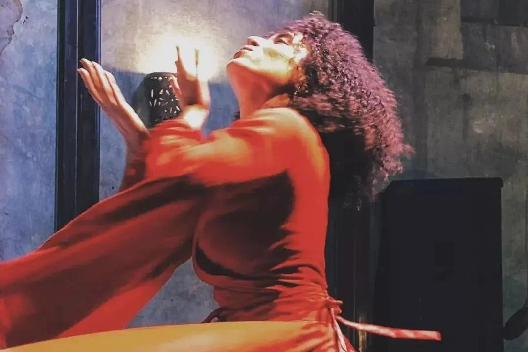 A woman with curly hair is lying down, propping her chin with her hand, looking upward contemplatively.