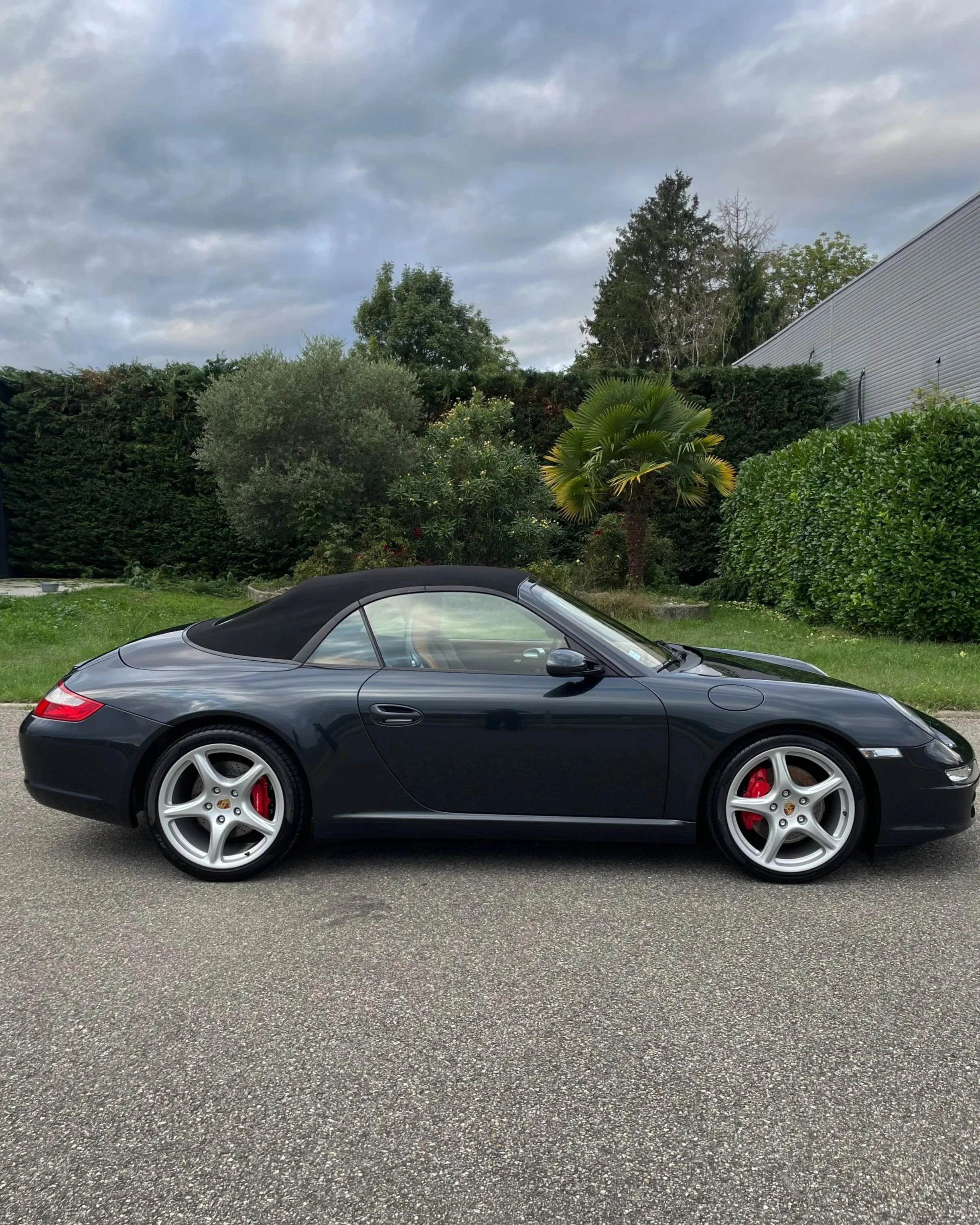 Voiture Porsche noire décapotable parked sur la chaussée, avec un ciel nuageux en arrière-plan.