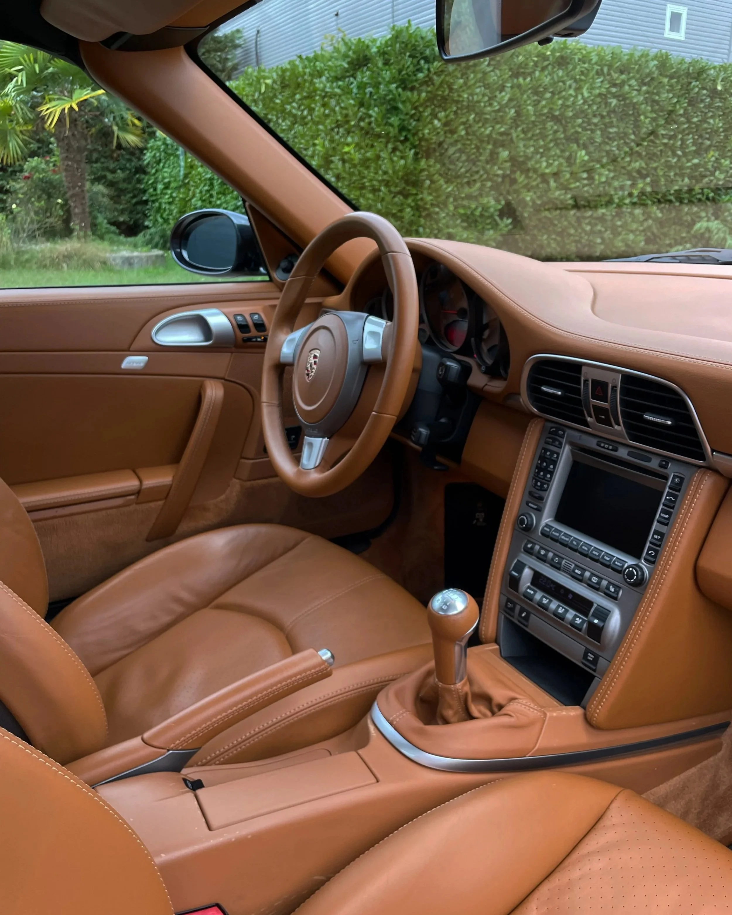 Intérieur d'une voiture de luxe Porsche avec un tableau de bord en cuir beige, un volant avec logo Porsche, un levier de vitesse et un écran de navigation central.