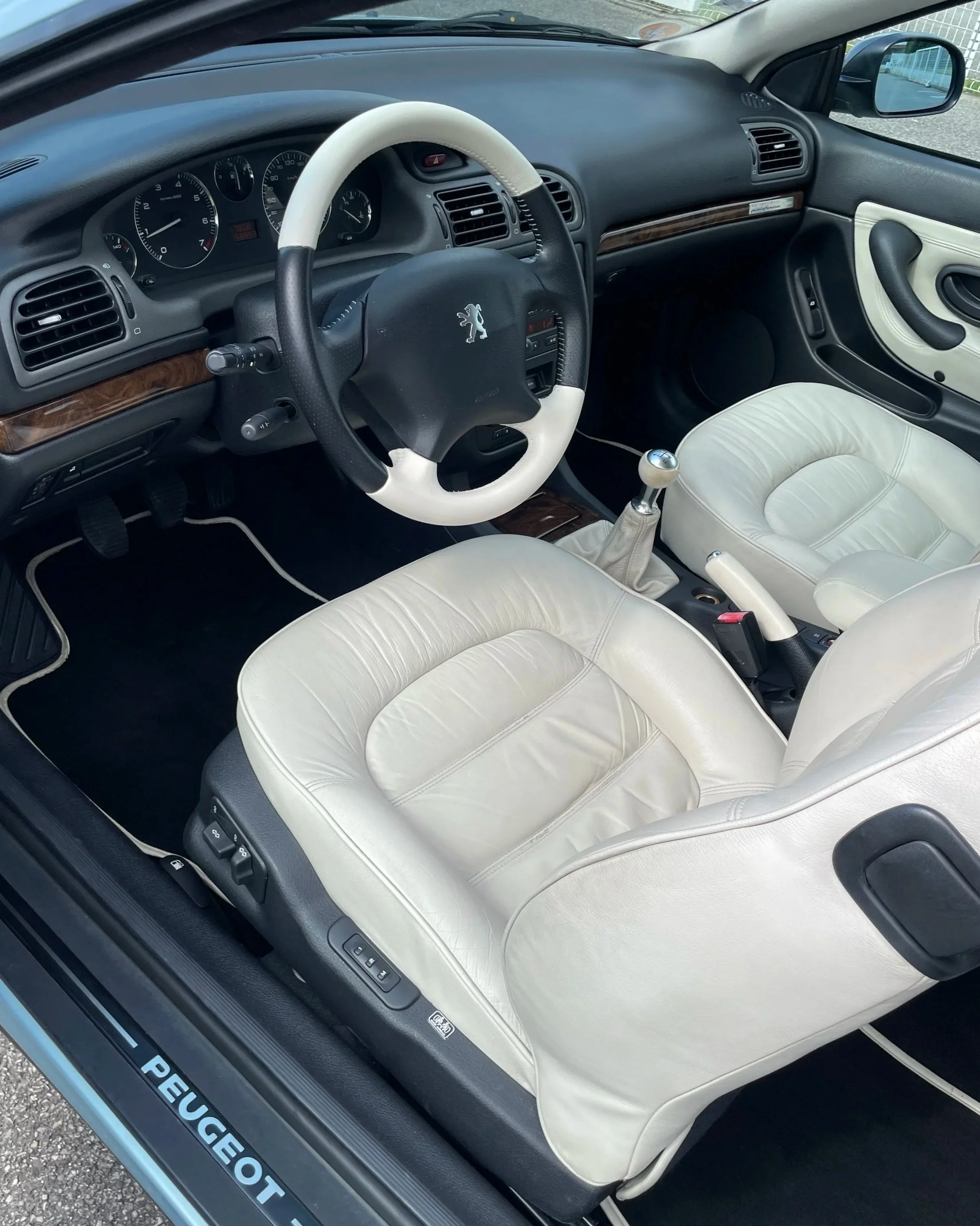 Intérieur d'une voiture Peugeot avec des sièges en cuir blanc, un volant noir et blanc, et un tableau de bord moderne.