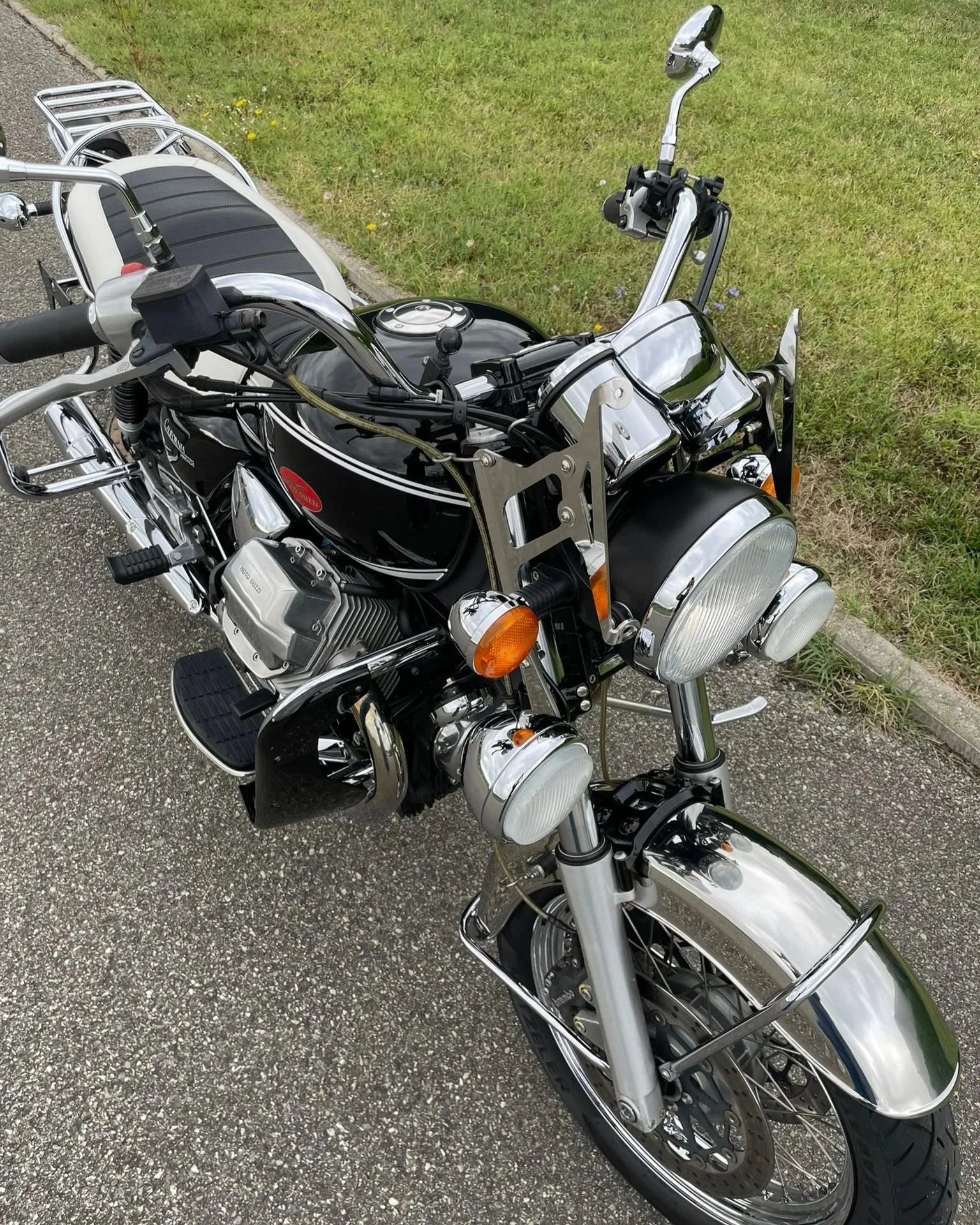 Moto noire avec des éléments chromés, stationnée sur le côté d'une route, avec un porte-bagages en aluminium derrière.