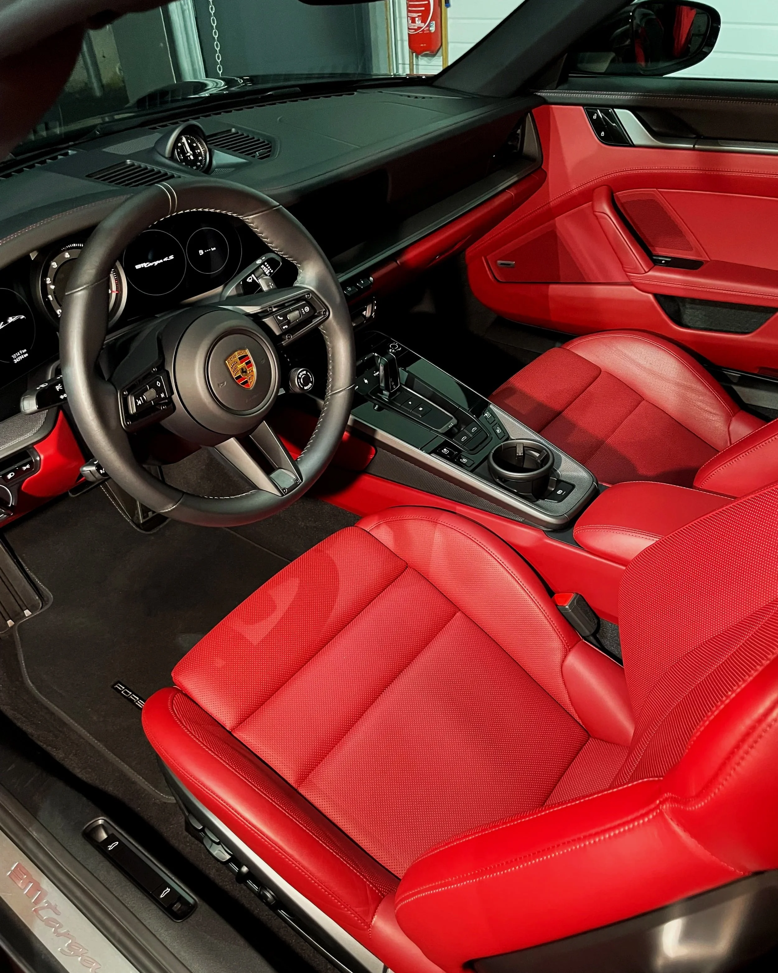 Intérieur d'une voiture Porsche, avec sièges et tableau de bord en cuir rouge et plusieurs écrans numériques.