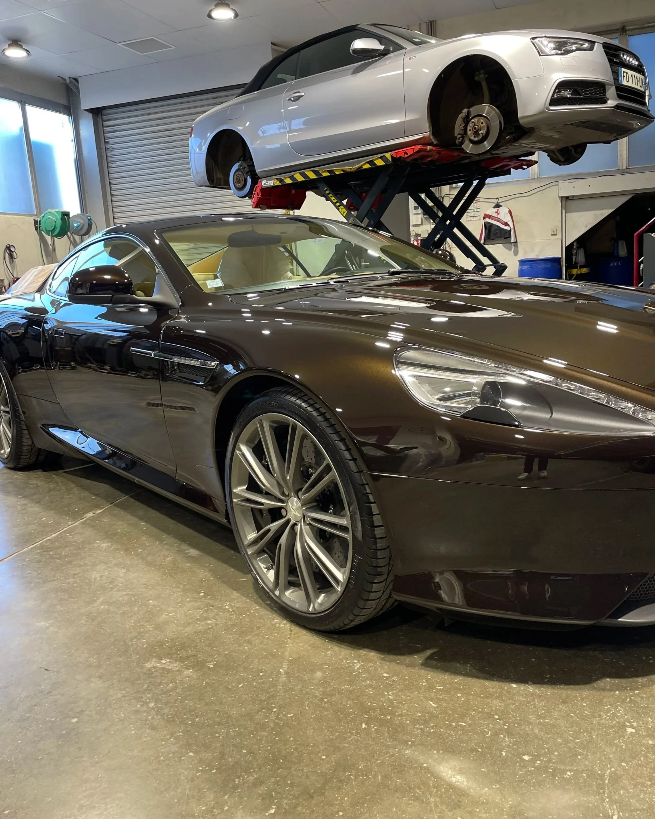 Deux voitures de luxe dans un garage, une noire à l'avant et une blanche sur un lift à l'arrière.