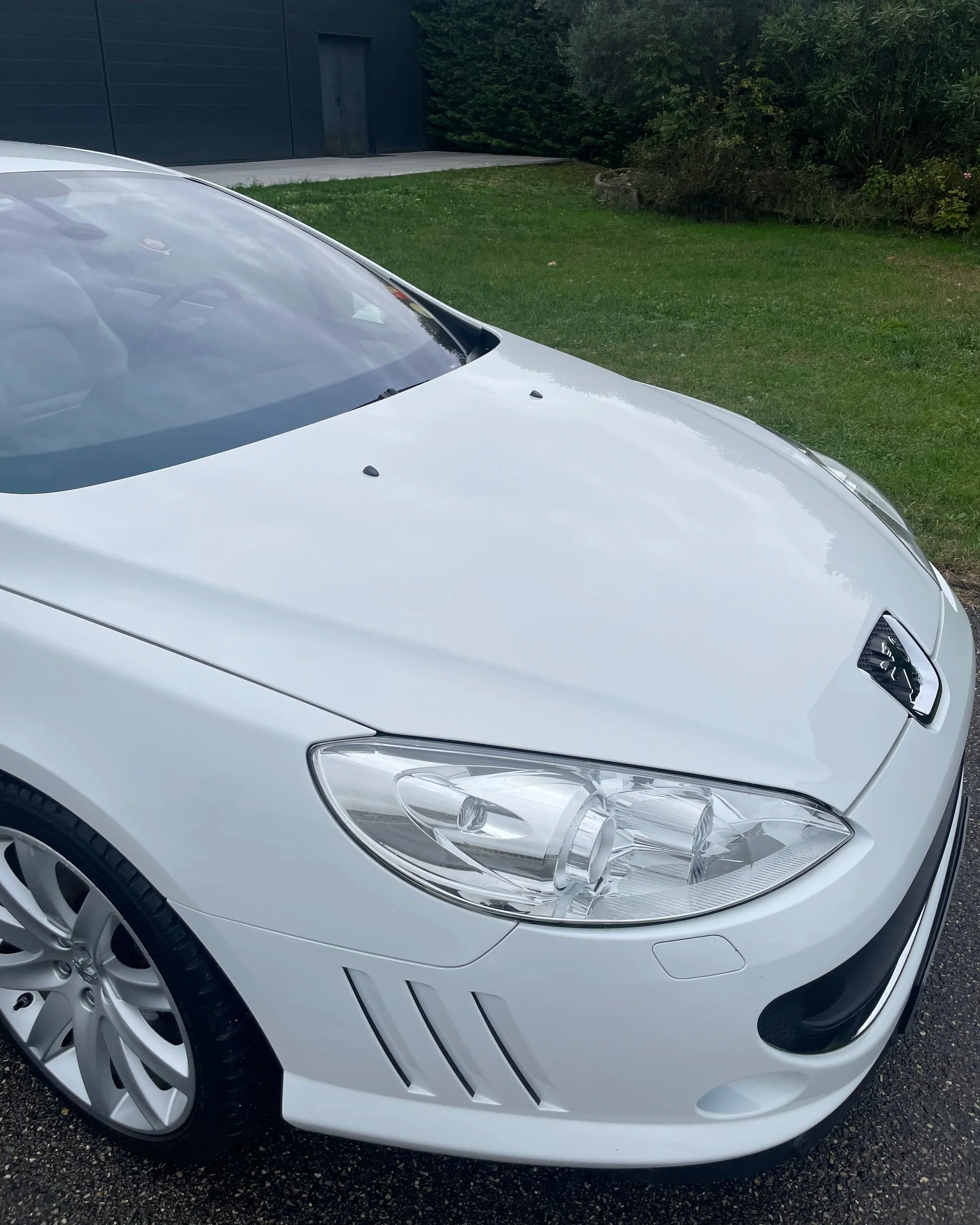 Voiture blanche devant une pelouse et un arbuste, vue de face