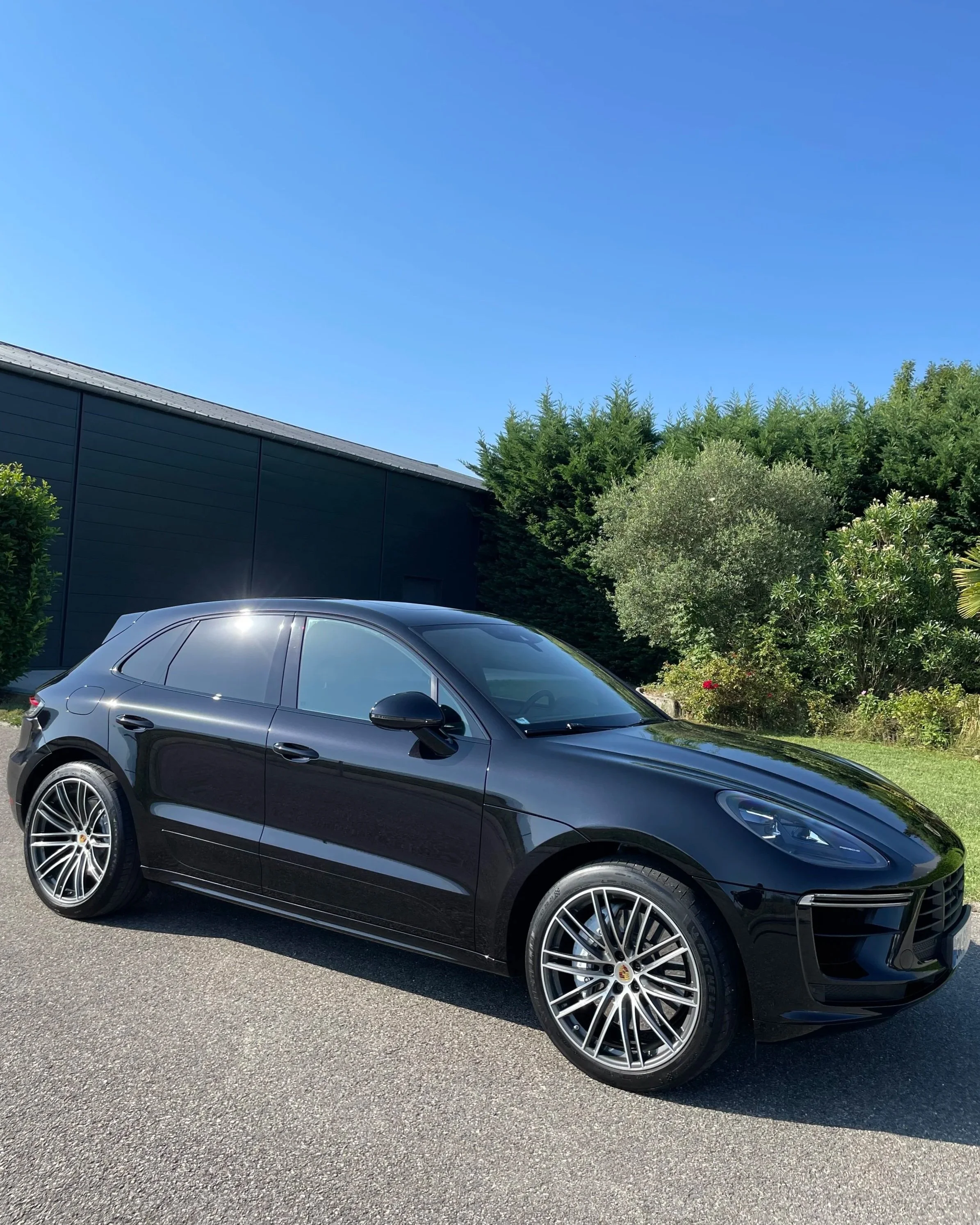 Voiture noire de luxe Porsche Cayenne garée sur une route en plein air avec un arrière-plan de végétation verte et un ciel bleu clair.