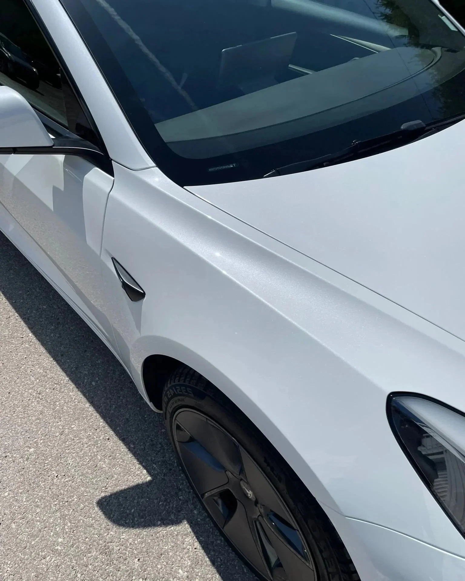 Voiture blanche vue de côté avec portière et roue half visible, stationnée sur une route ensoleillée.