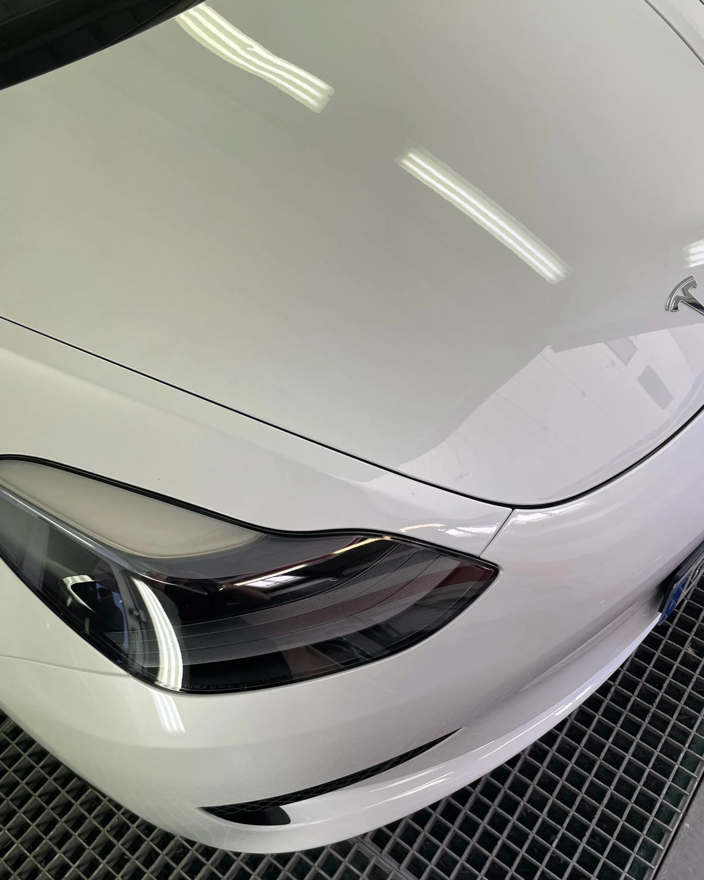 Vue partielle d'une voiture blanche, montrant le capot, le phare avant et une partie du pare-chocs avant.