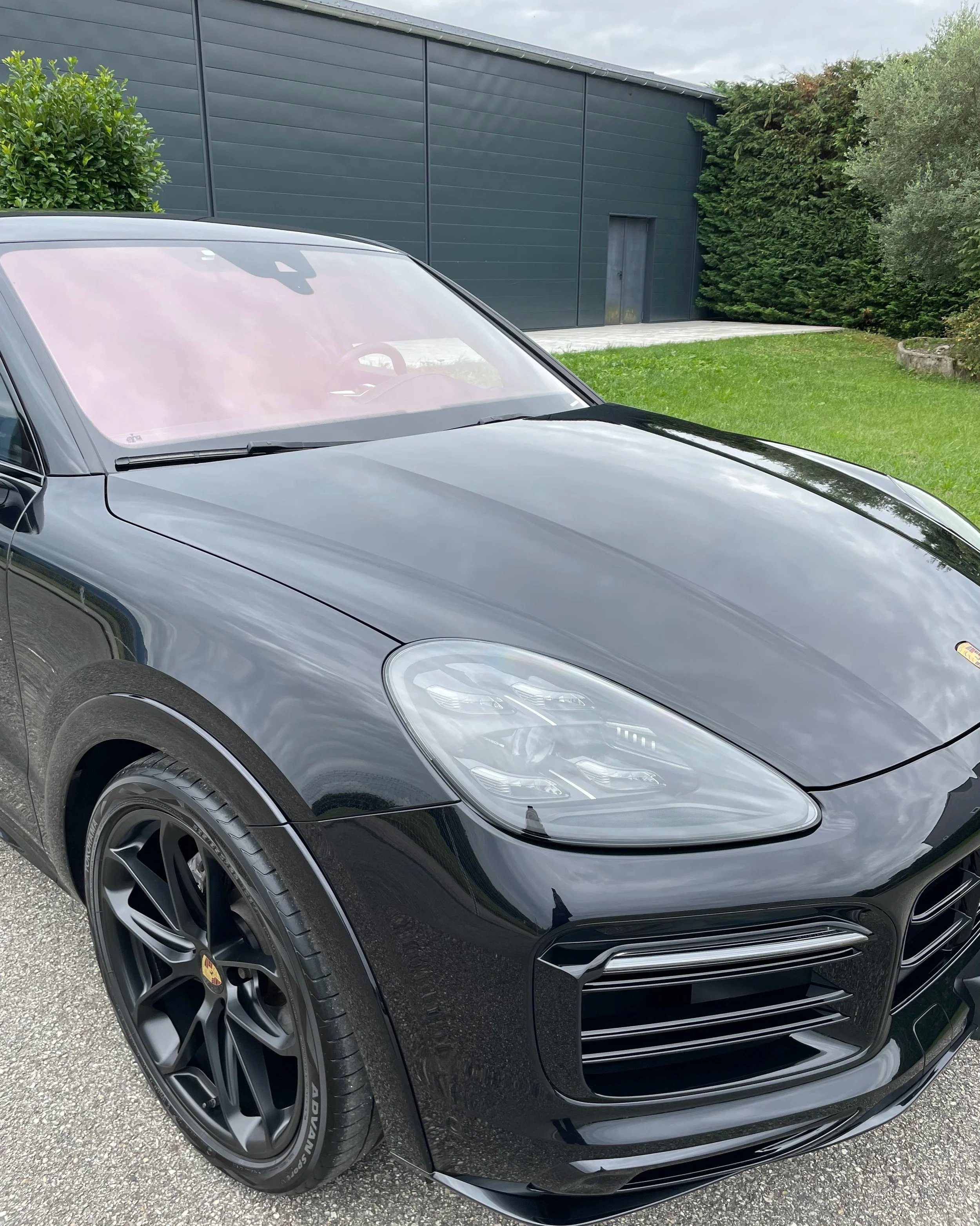 Voiture noire de luxe Porsche Cayenne devant un bâtiment moderne avec un jardin vert.