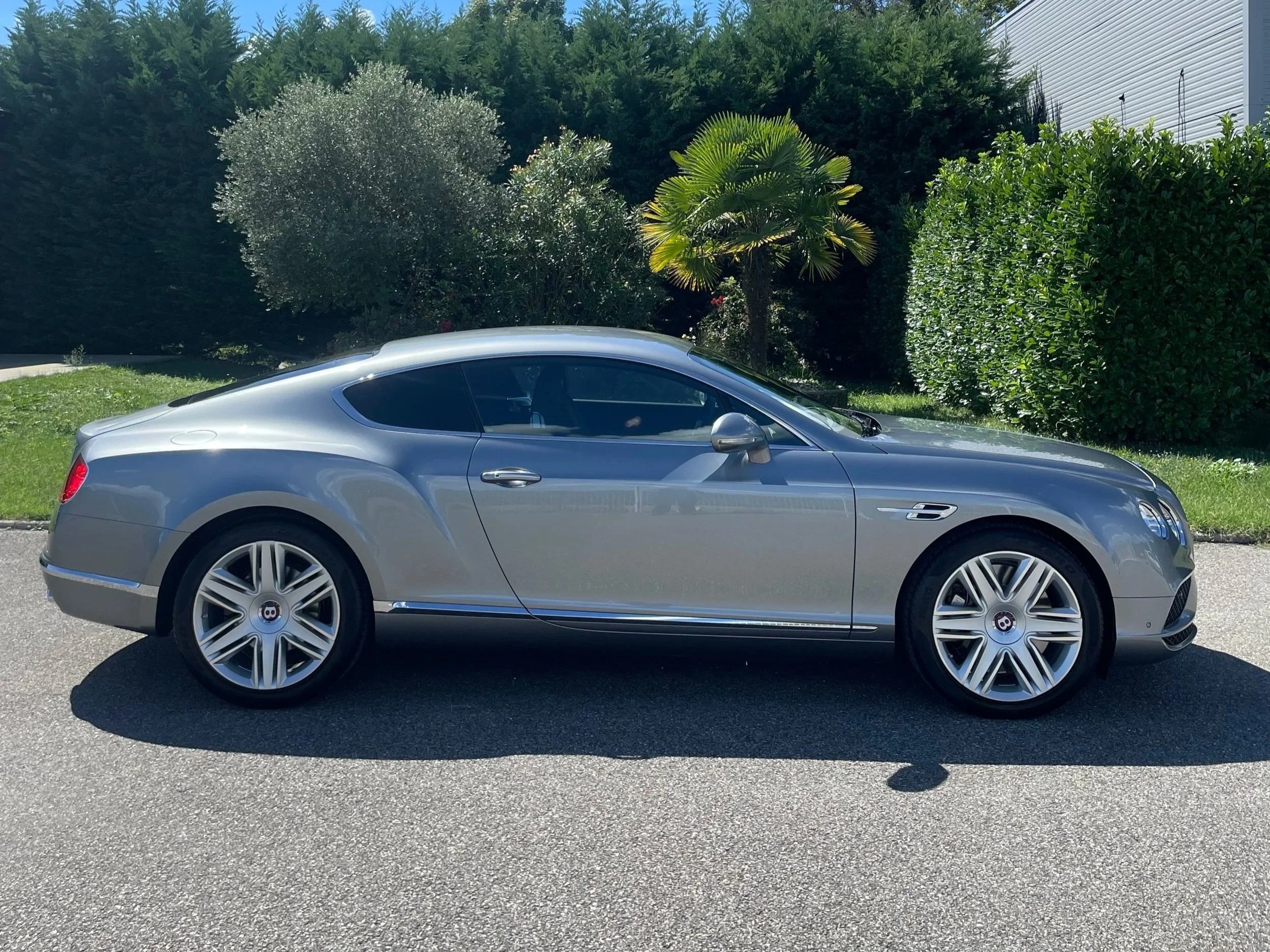 Voiture de luxe grise stationnée sur la route avec des arbres et un bâtiment en arrière-plan.