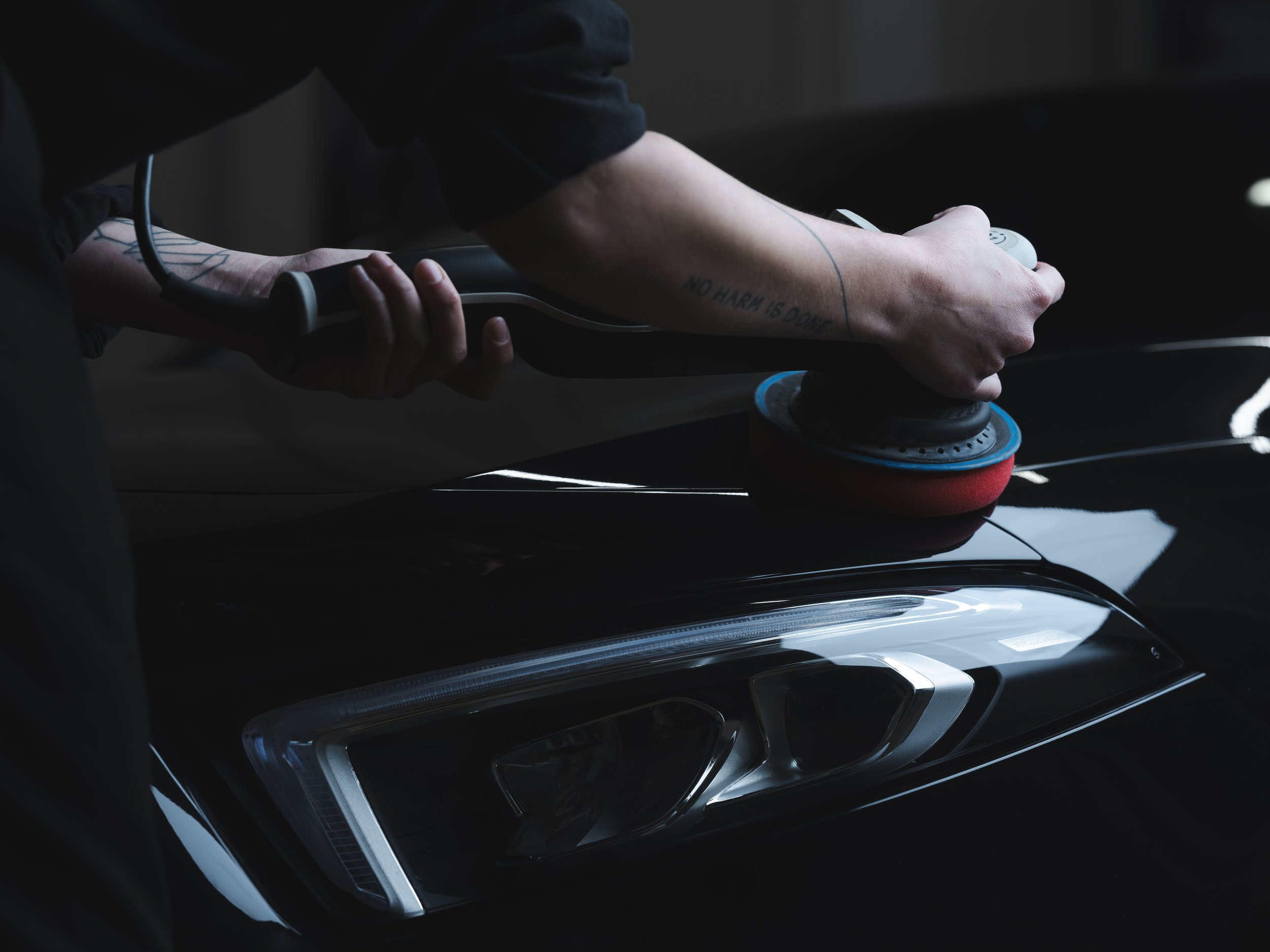 Une personne utilise une machine à polir les phares d'une voiture noire.