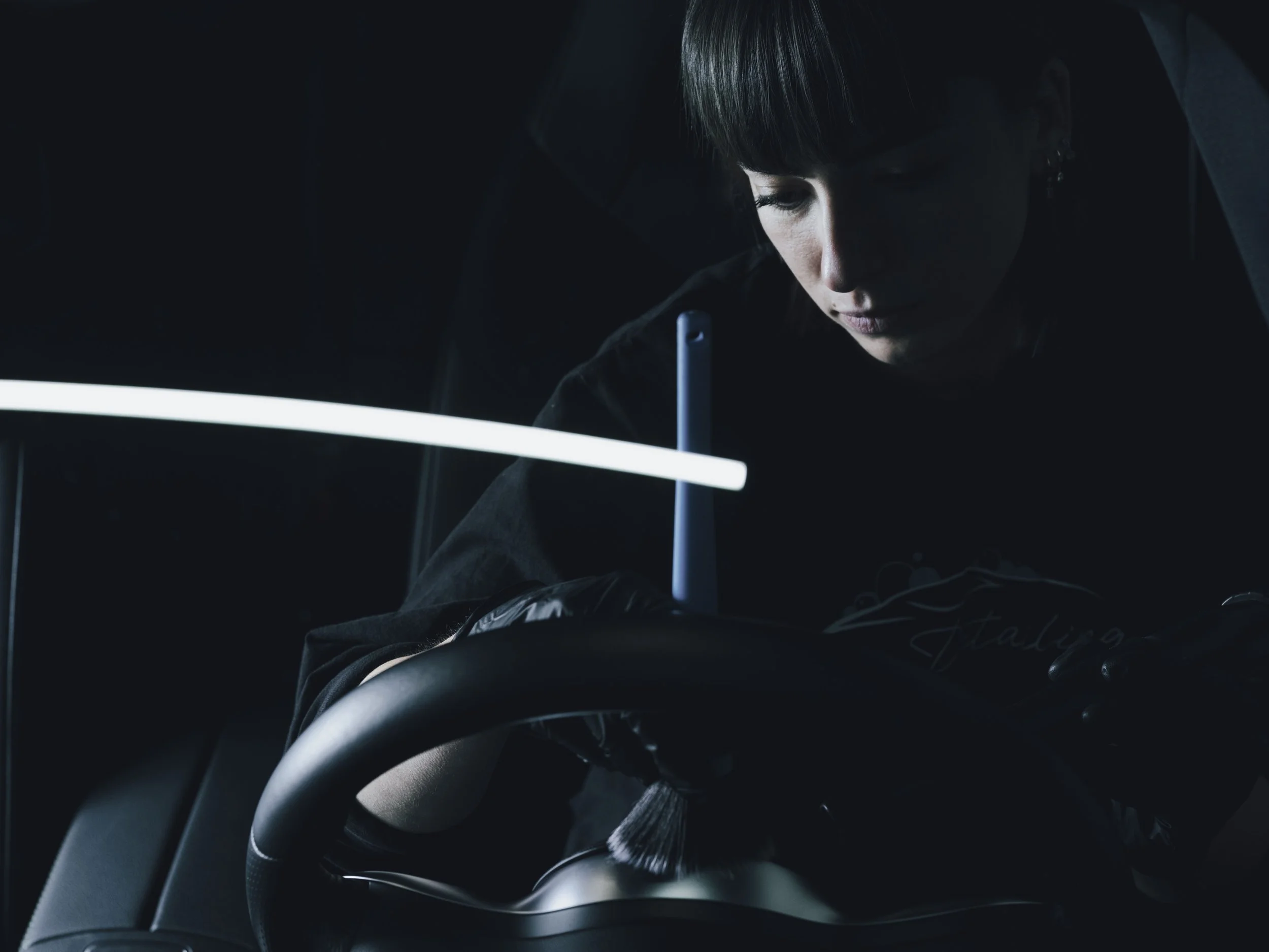 Une femme à l'intérieur d'une voiture sombre, concentrée sur ce qu'elle fait, avec un éclairage minimal mettant en valeur son visage et ses mains