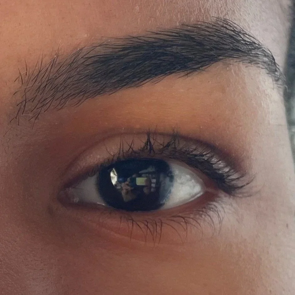 Close-up of a human eye with dark brown iris, surrounded by skin and eyelashes. Thick healthy eyebrows post wax with Nu-Free soy-based wax.