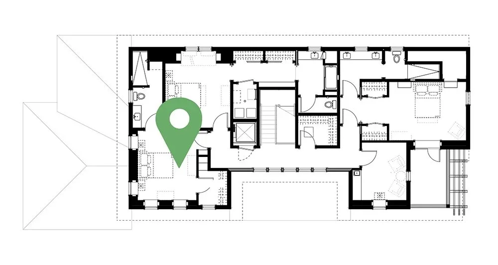 Floor plan of a house with a green location marker near the center, showing rooms, hallways, stairs, and exterior doors.