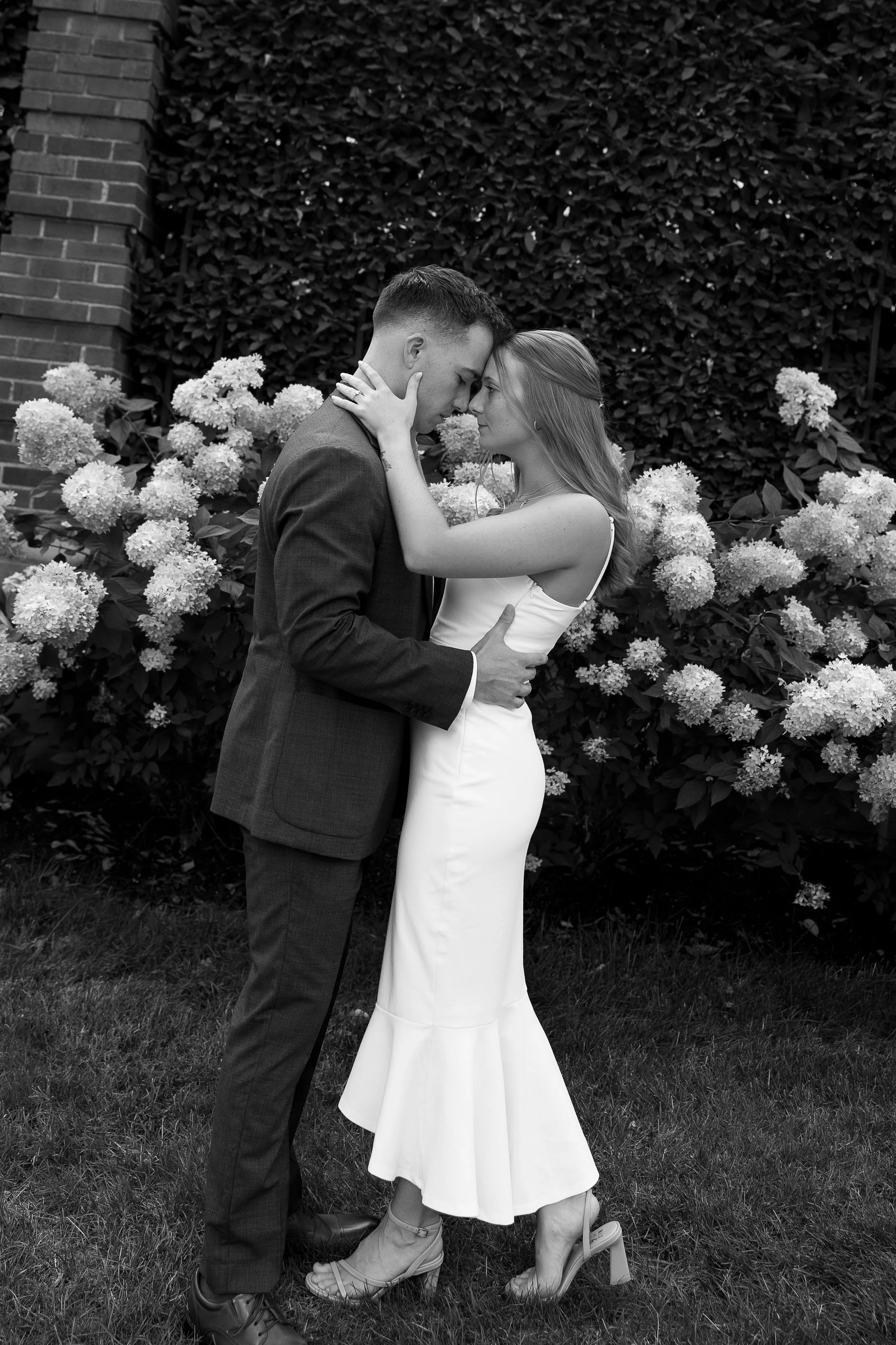 Pittsburgh wedding couple share a candid embrace beside white hydrangeas, black and white documentary photo