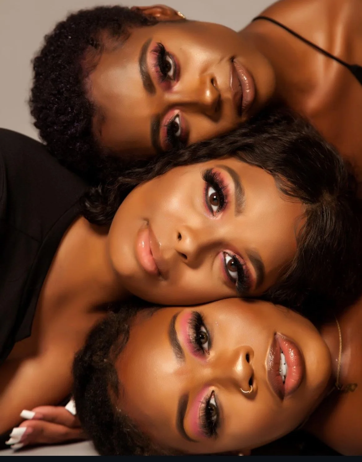 Four women with diverse skin tones and makeup lying close together, with their heads touching in a portrait shot.