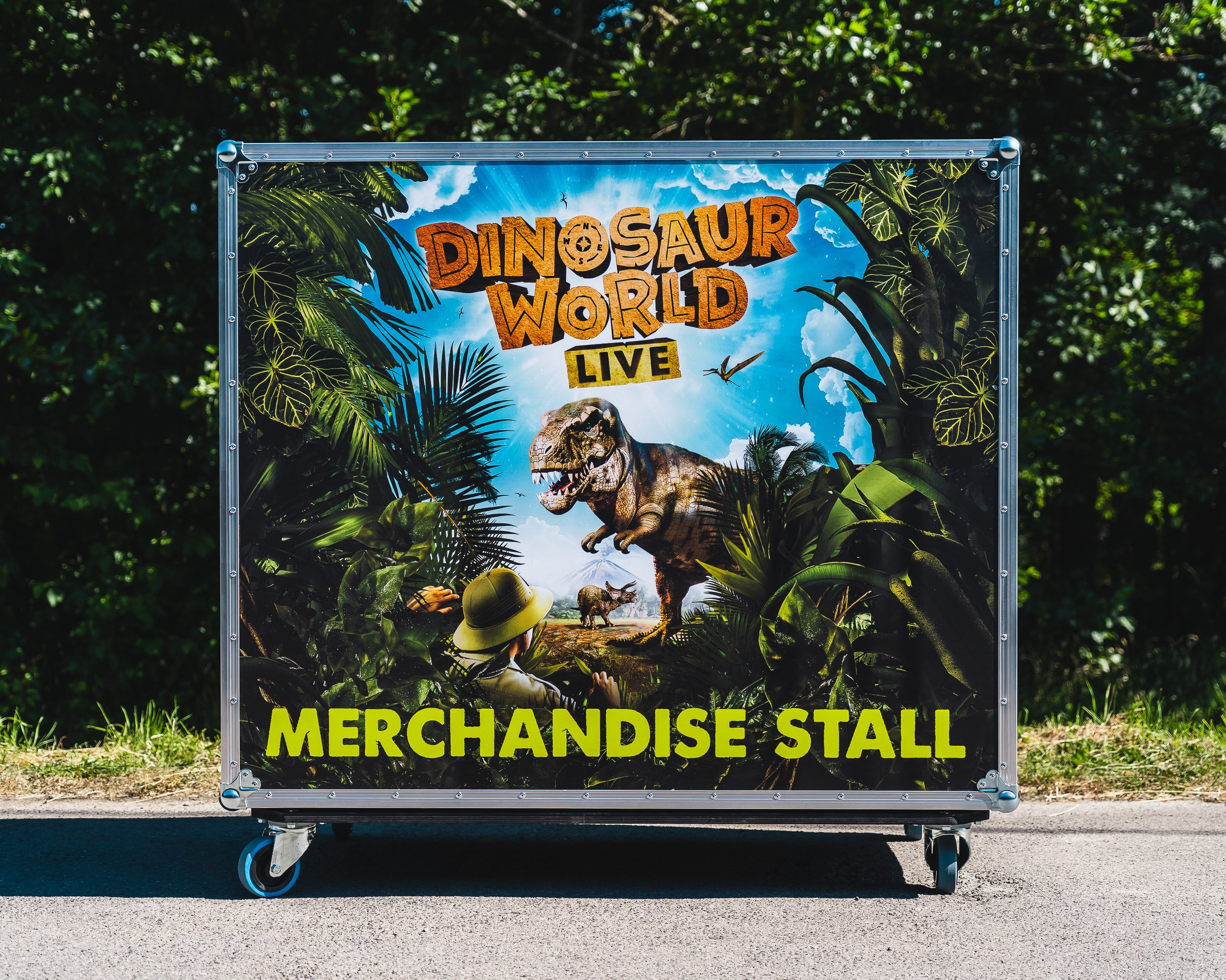Poster for "Dinosaur World Live" featuring dinosaurs and jungle scenery, advertising a merchandise stall.