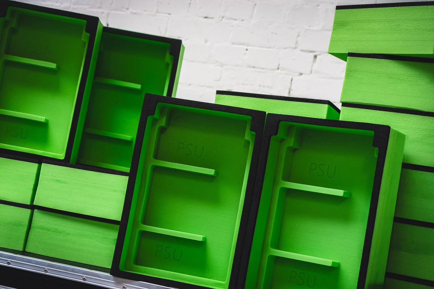Green PSU foam inserts stacked against a white brick wall.