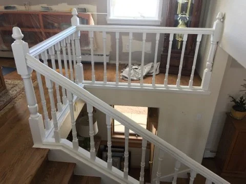 White staircase railing with orange carpet on the stairs, adjacent to a door and potted plant in a room with hardwood floors.