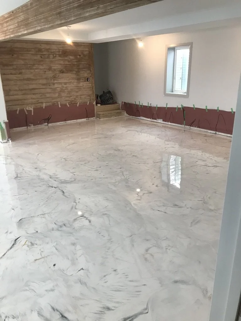 Room under renovation with a polished marble floor, partially finished drywall with wood paneling, and an open window.