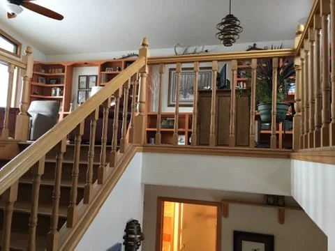 Interior view of a staircase leading to an upper-level living area with bookshelves, chairs, and potted plants.