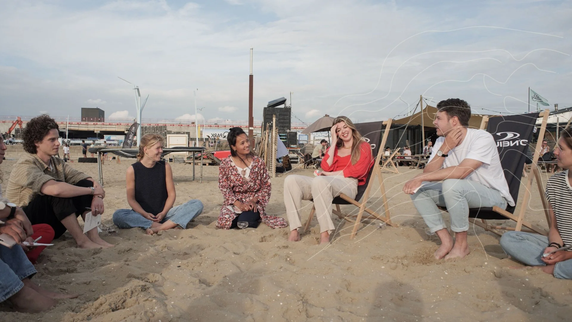 Groep mensen zittend op zand op het strand, lachend en pratend.