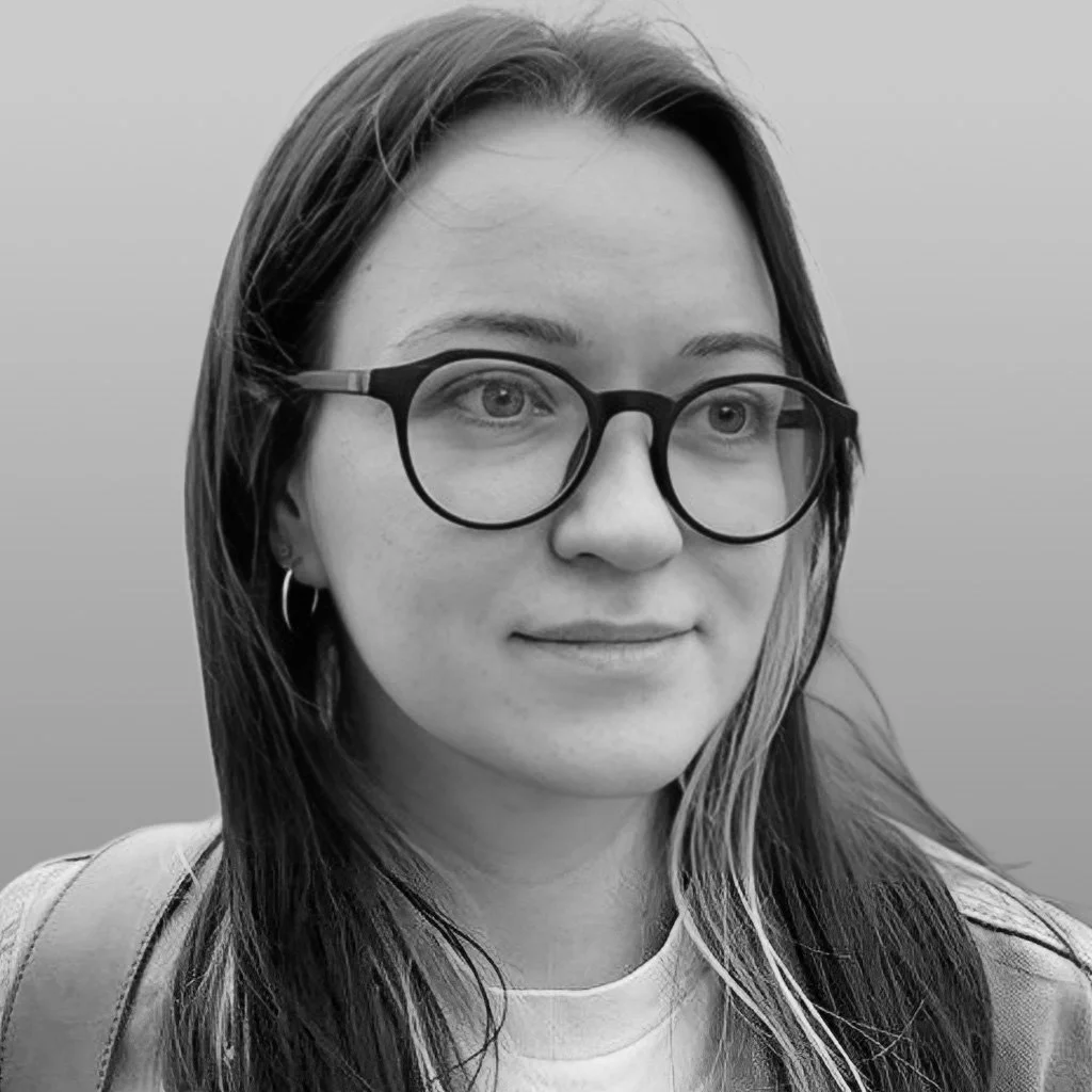 Black and white photo of a young woman with long hair, glasses, hoop earrings, and a slight smile.