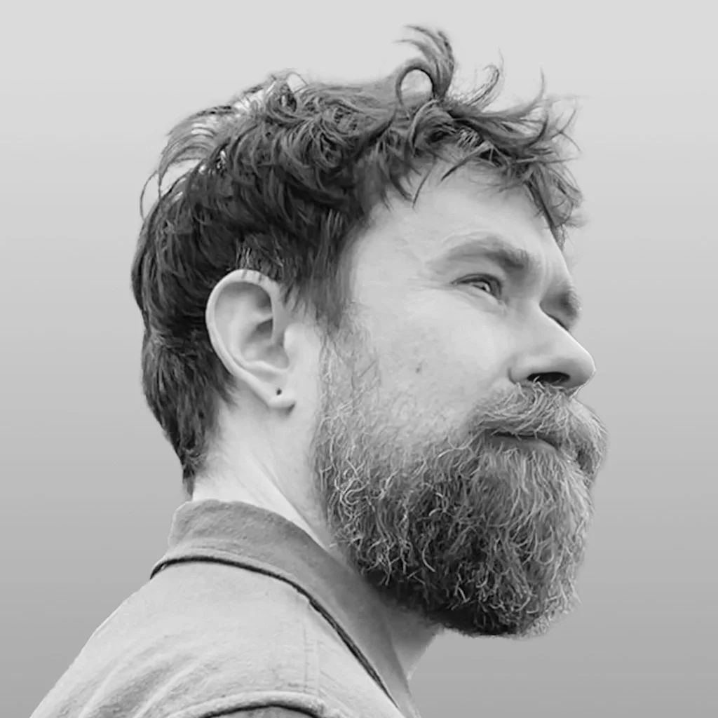 Black and white photo of a man with a beard and curly hair, facing to the right with a contemplative expression.