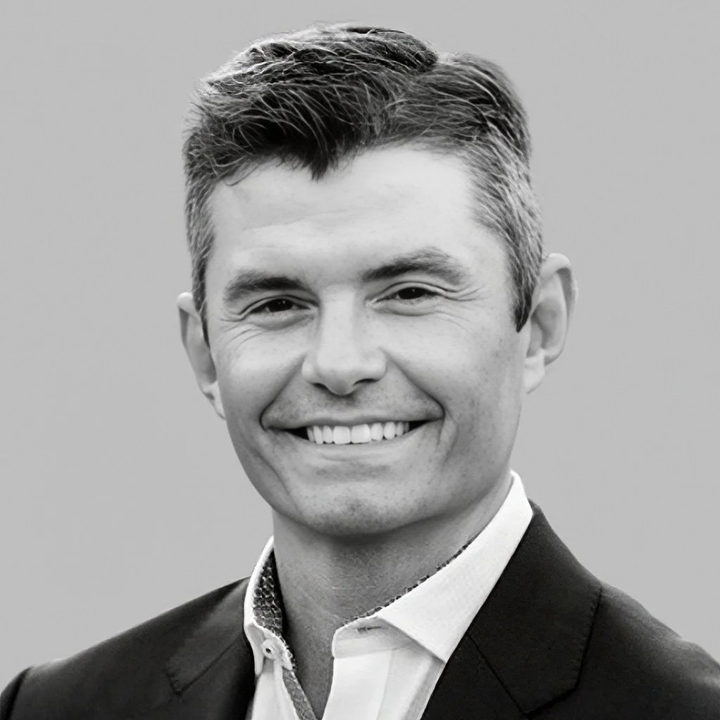 Black and white headshot of a smiling man wearing a suit and white shirt.