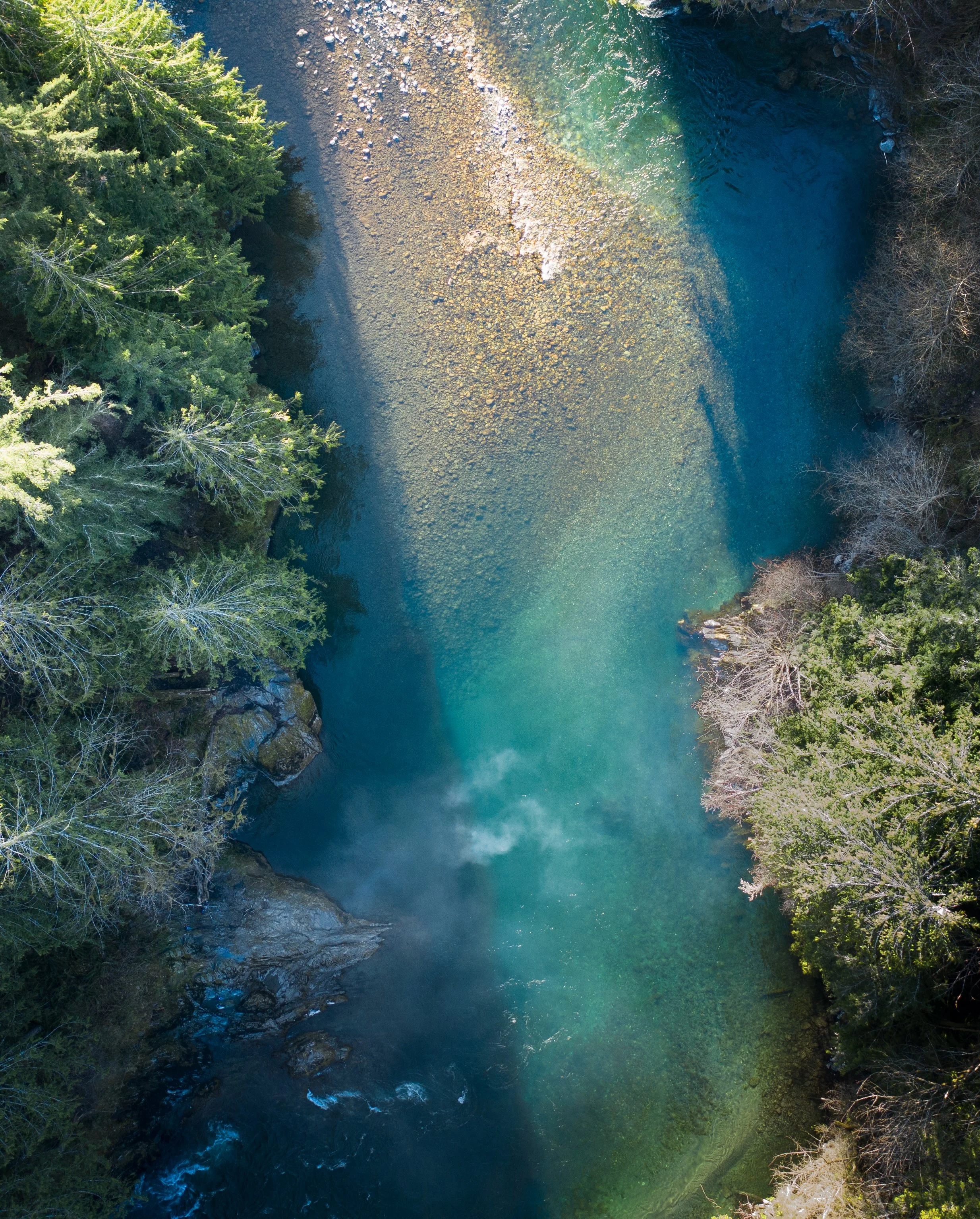 An aerial view of a river flowing through a forest, with clear blue-green water and trees on both sides.
