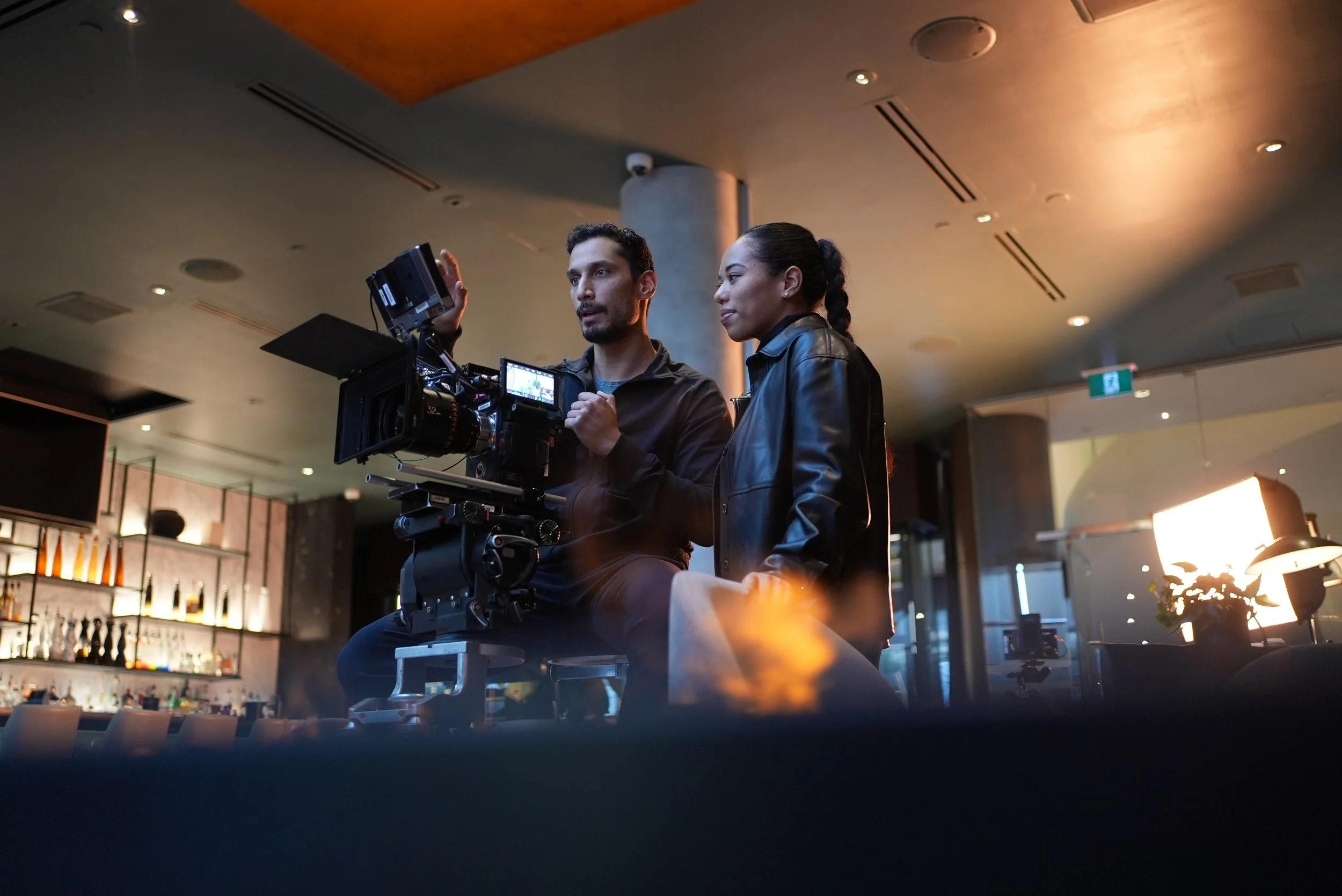 Two people discussing a professional camera on a film set or shoot in a modern indoor setting.