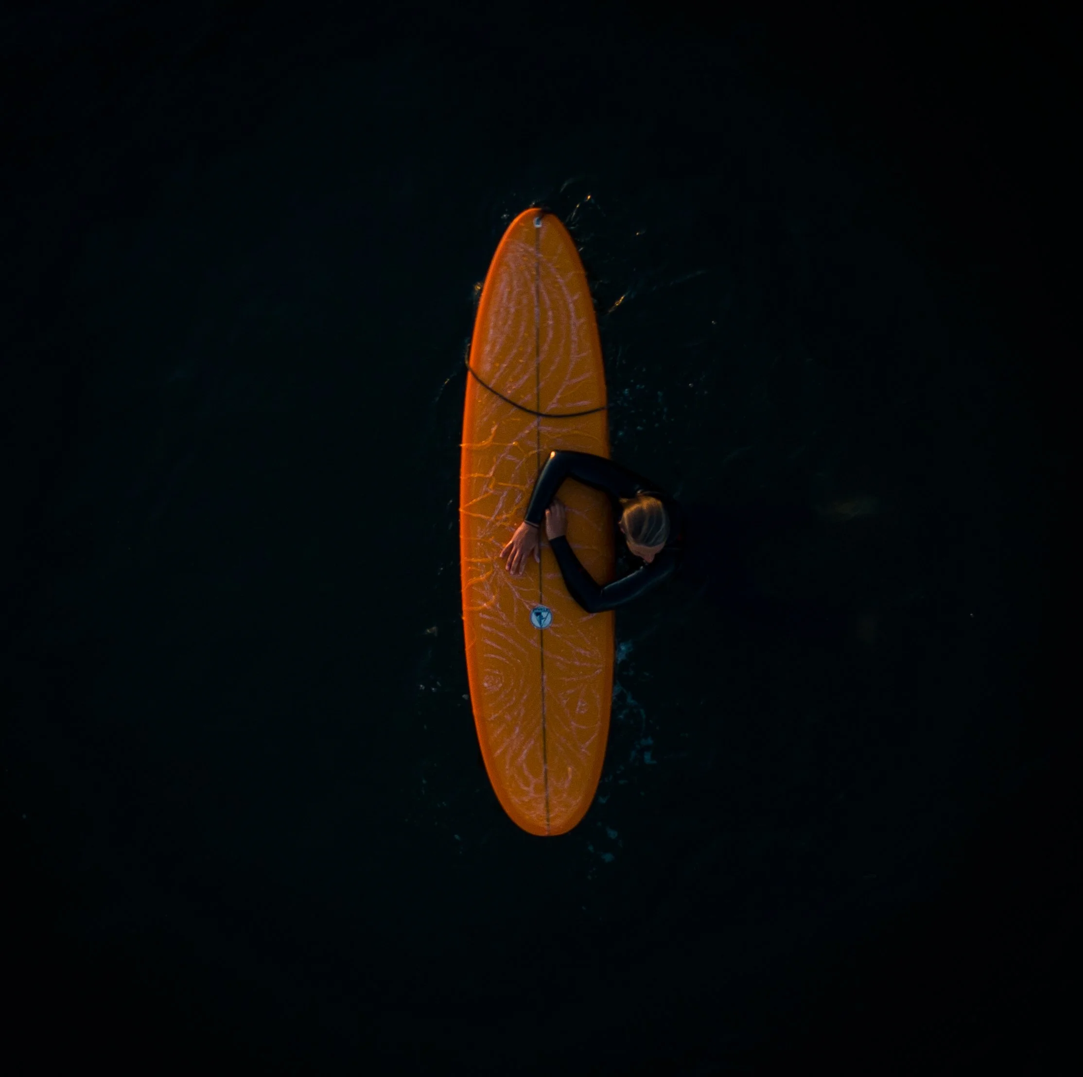 Person with blonde hair in a wetsuit riding an orange paddleboard on dark water.
