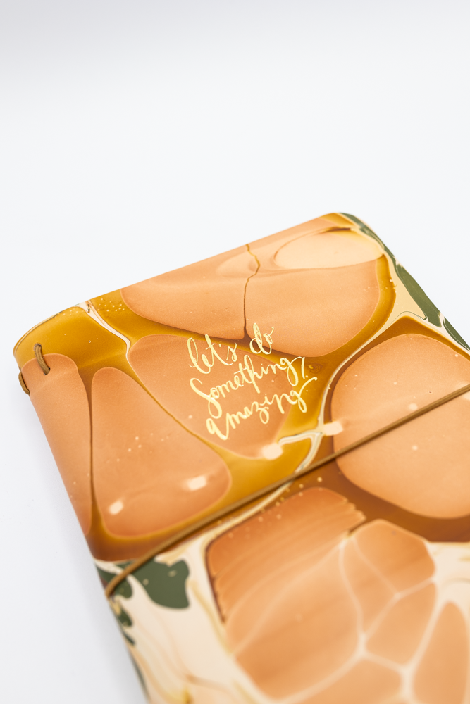 Notebook with marbled cover and the text 'Let's do something amazing!' in calligraphy style.