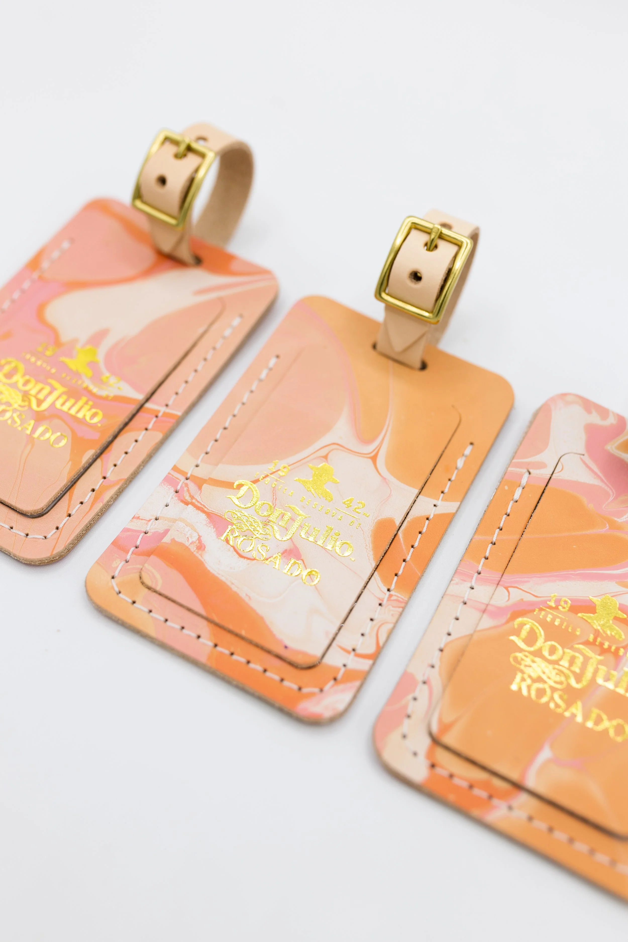 Three marbled leather luggage tags with gold lettering and buckles.
