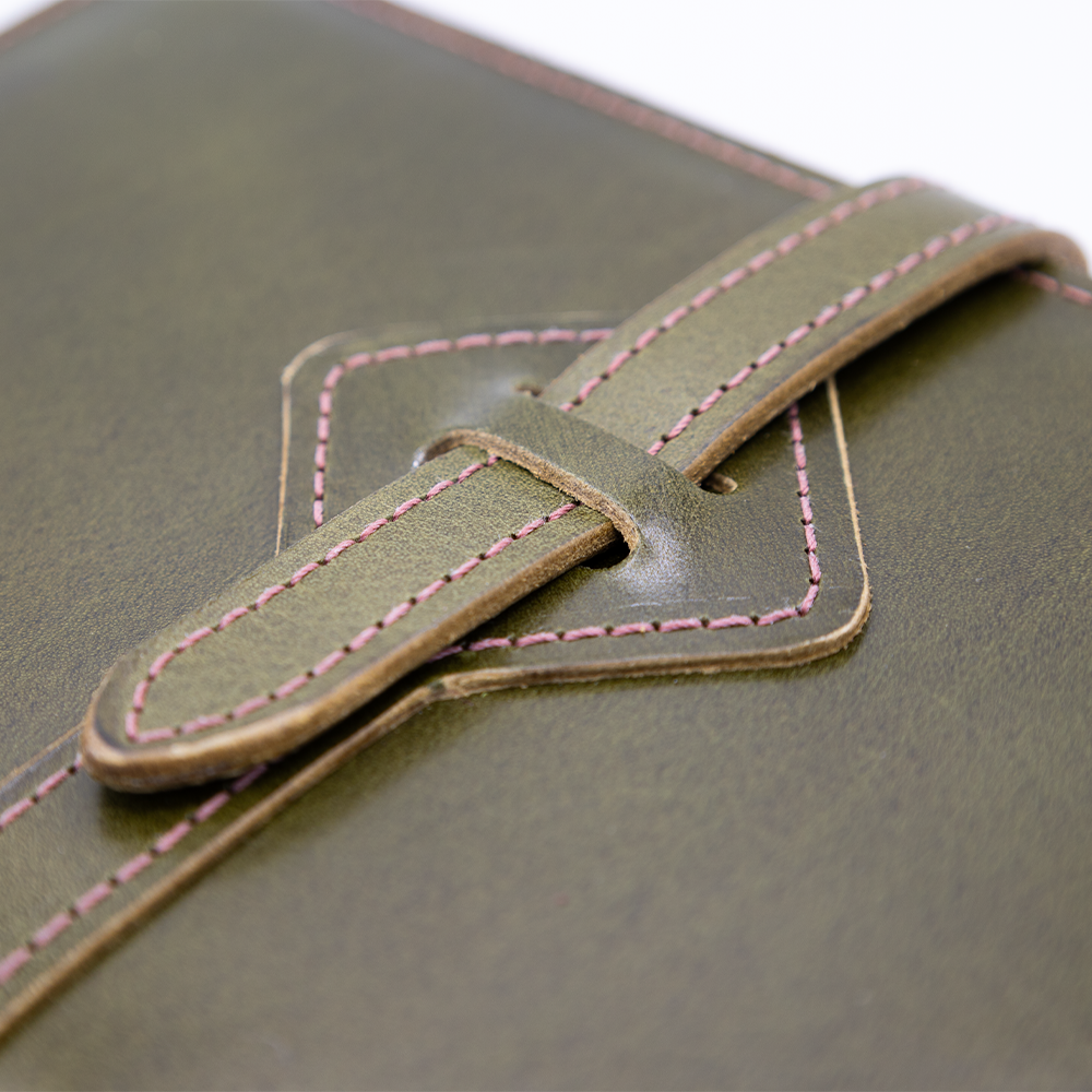 Close-up of a green leather journal with a strap and pink stitching detail.