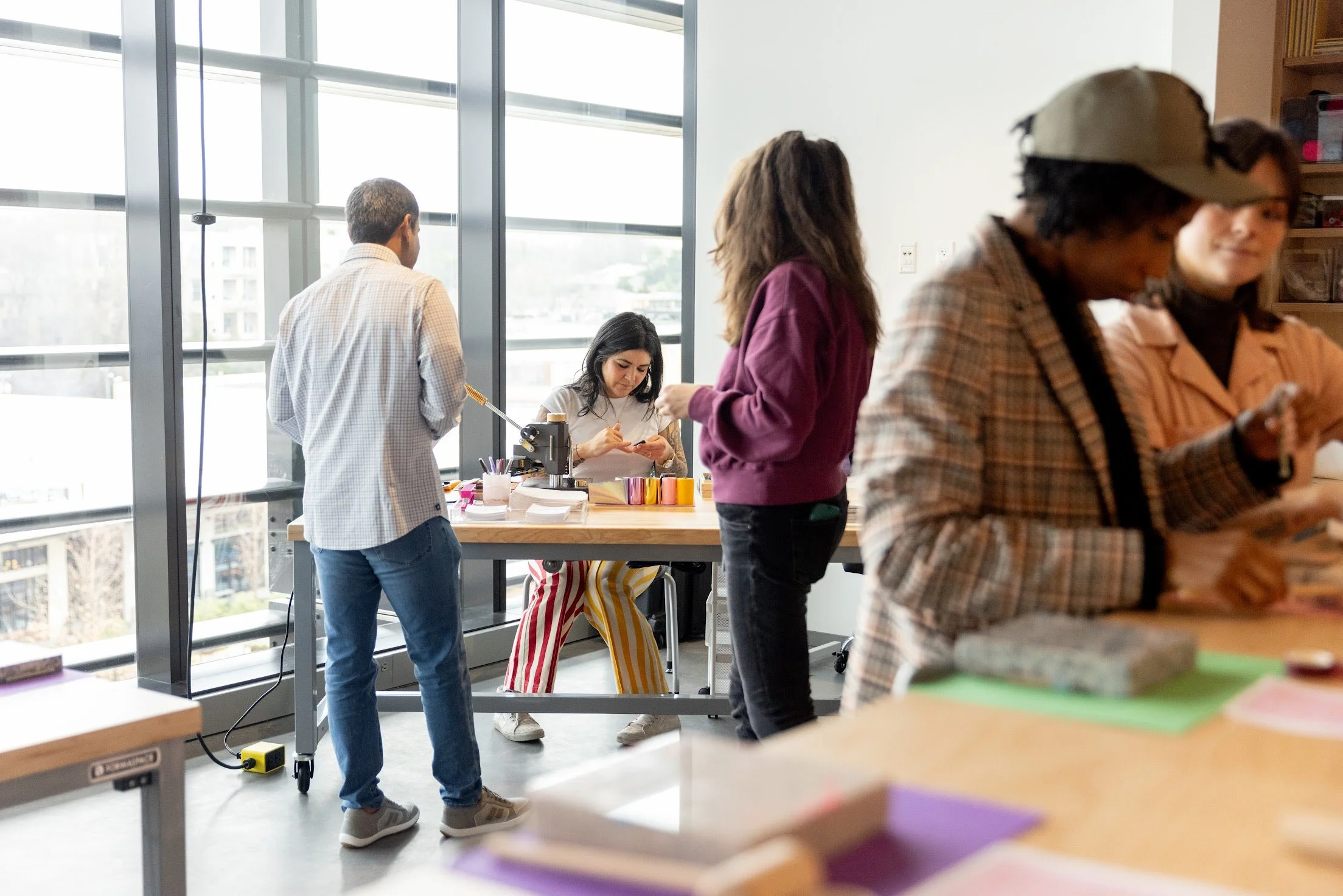 Group of diverse people engaged in a creative workshop in a well-lit room with large windows.