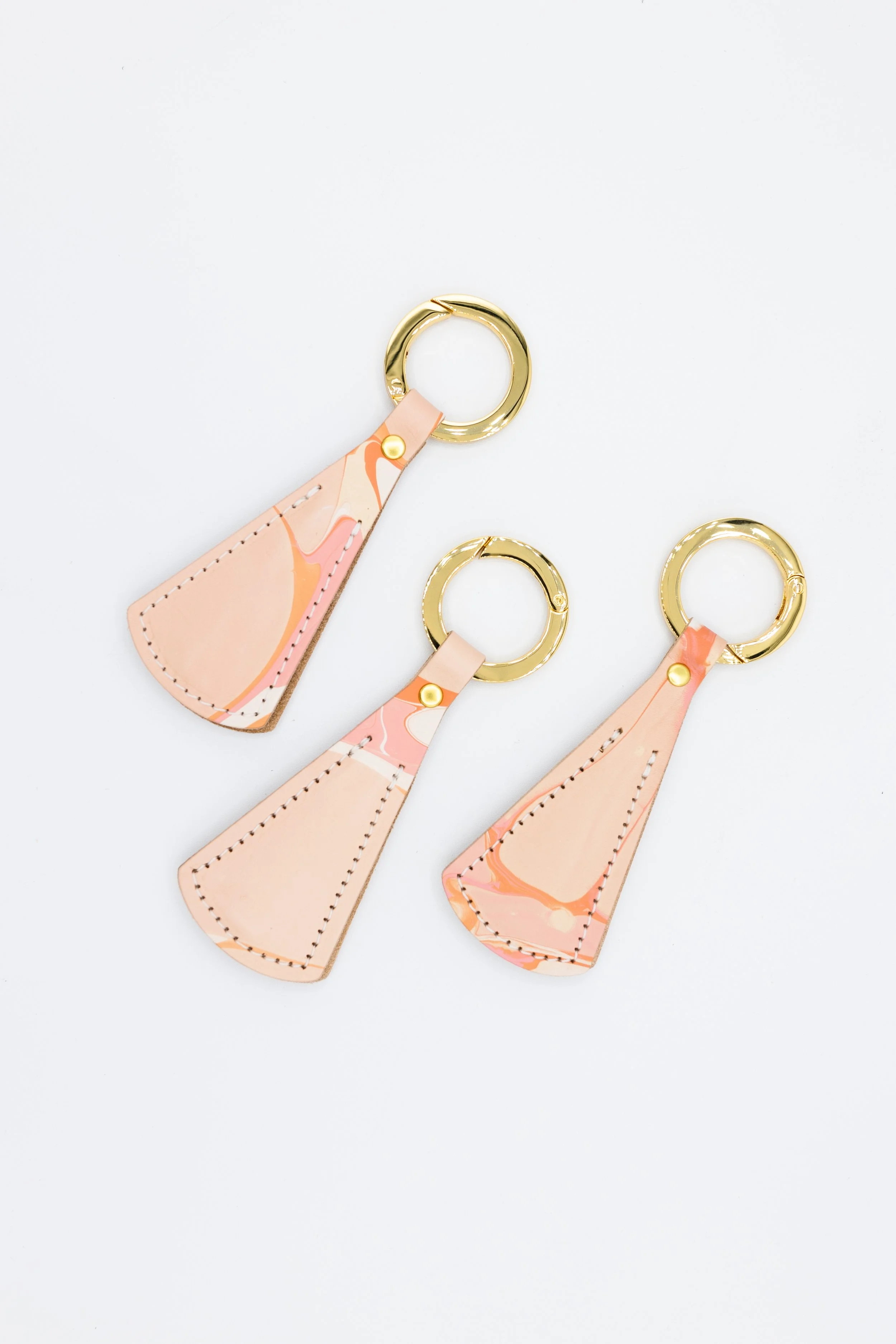 Three leather hat clips with pink and orange marbled patterns and gold rings on a white background.