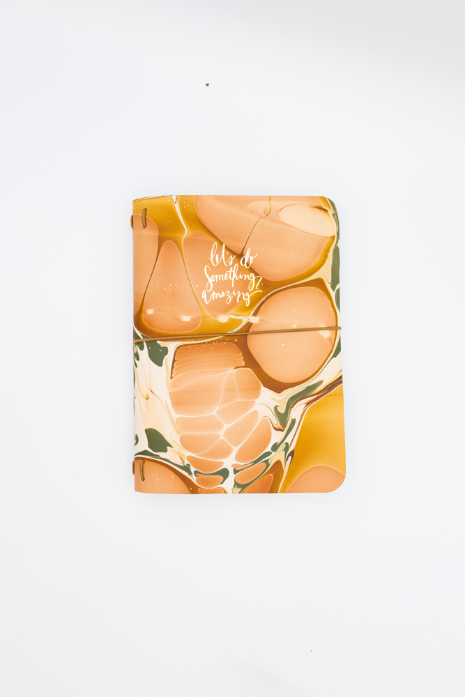 Leather notebook with abstract orange and beige marble cover design and 'let's do something amazing' text.