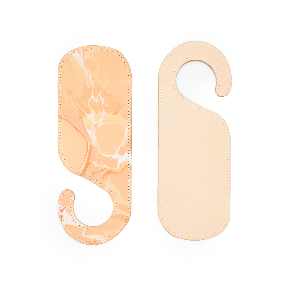 Two leather door hangers, one with a marbled orange and white design, the other plain beige, both with hook-like shapes.