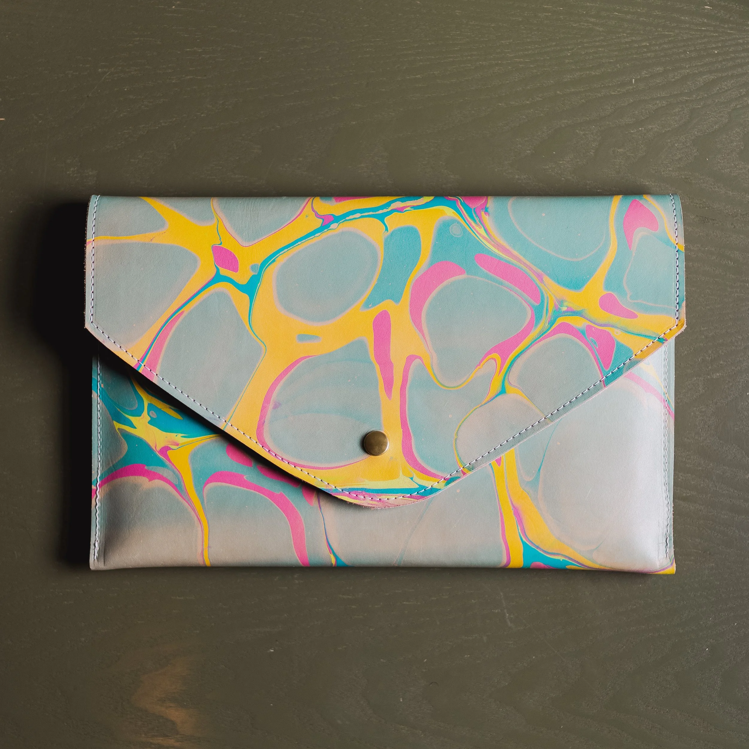 Colorful envelope clutch with abstract marbled design on green background
