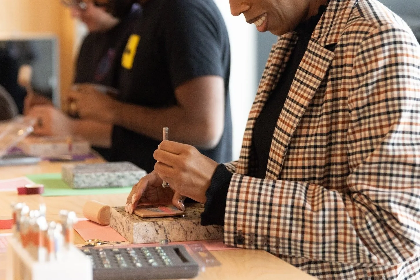 People engaged in crafts at a table, focusing on a plaid-suited person using a tool on a stone block.