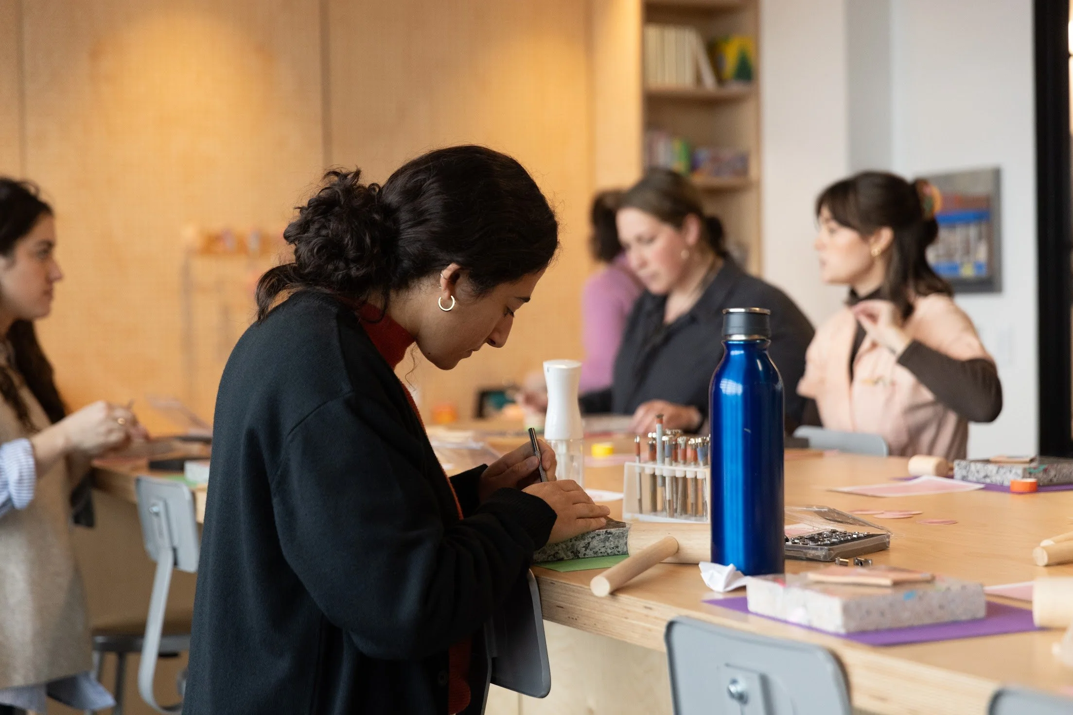 People engaged in a craft activity at a worktable with tools and materials.
