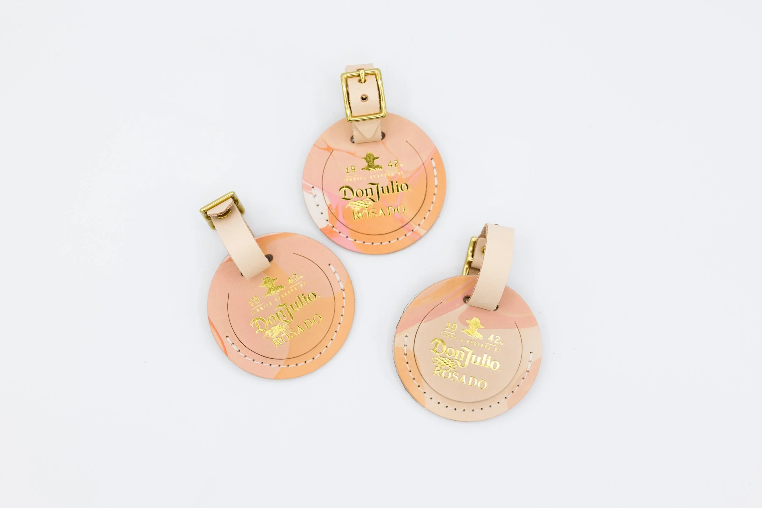 Three round leather luggage tags with gold embossed text "Don Julio Rosado 1942," featuring buckled straps on a white background.